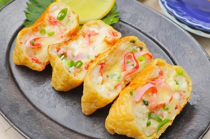 お皿に盛られた稲荷寿司、ネギやカニカマが詰められている。レモンが添えられている。