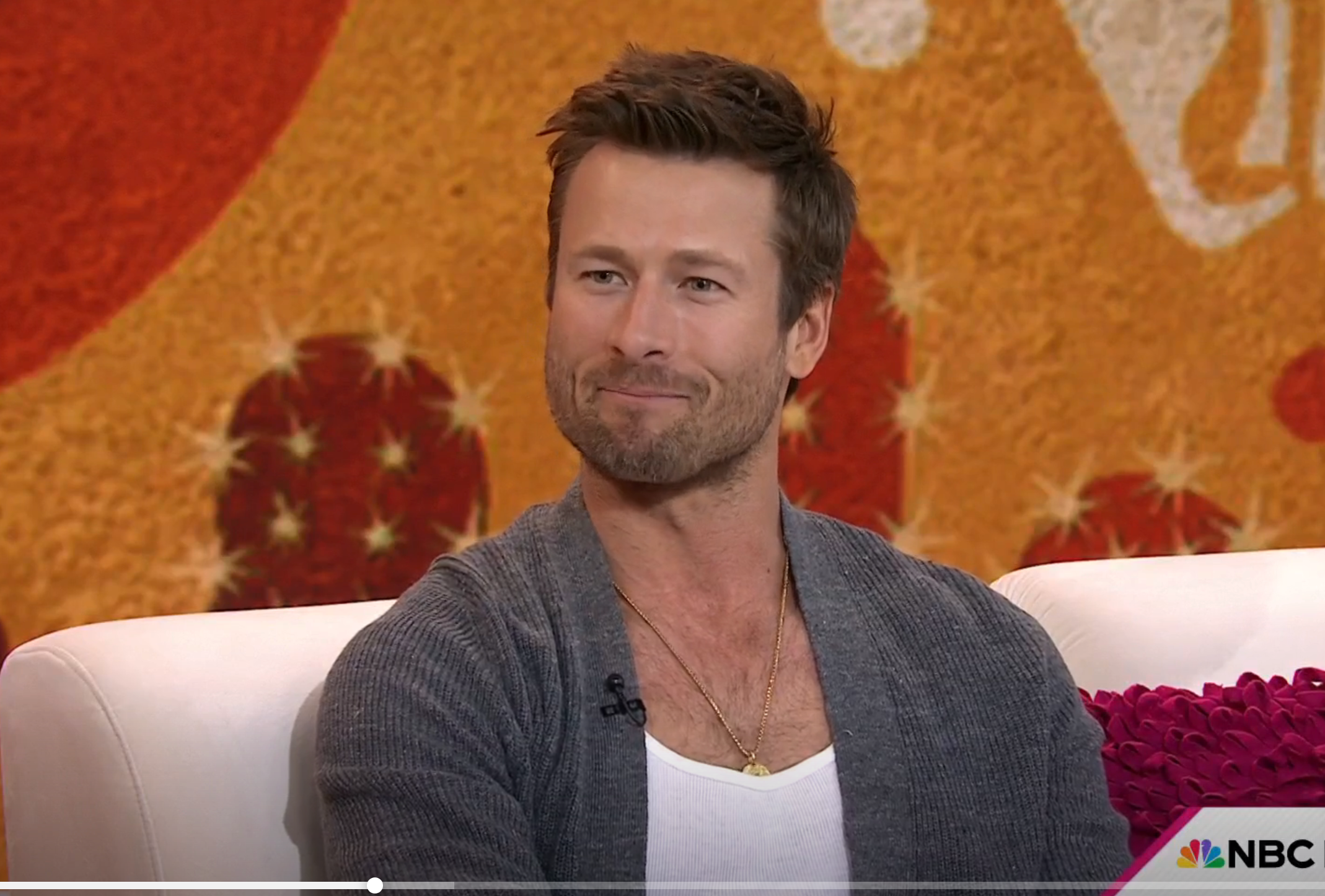 Glen Powell sitting on a talk show couch, engaged in conversation