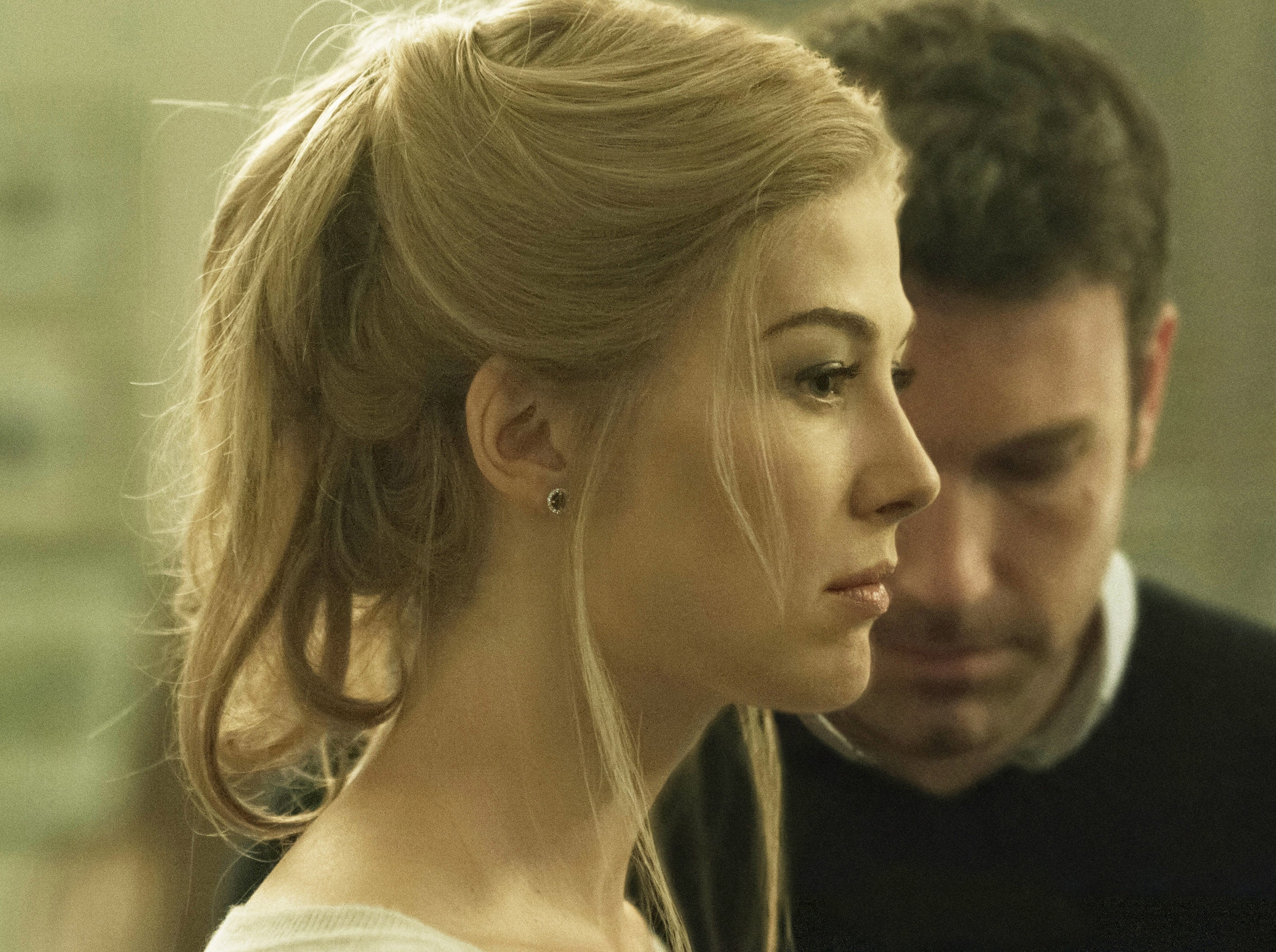 Rosamund Pike and Ben Affleck as Amy and Nick in "Gone Girl," tense scene, Amy looks to the right while Nick looks down behind her