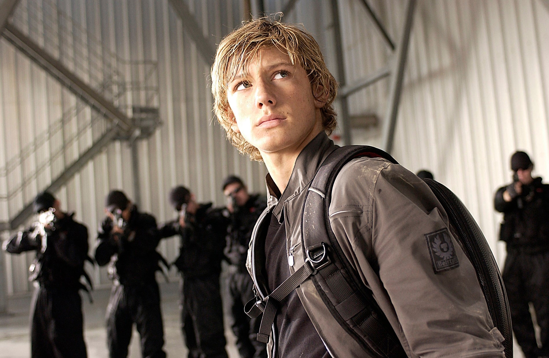 Alex Pettyfer as Alex Rider in "Stormbreaker" with armed soldiers pointing guns at him in the background as he stares off into the distance