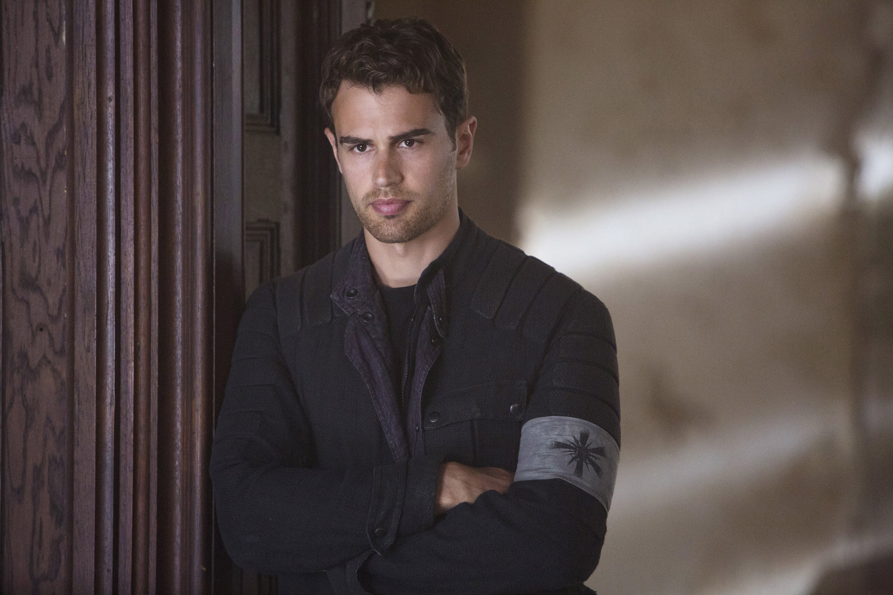 Theo James in "Divergent" leaning against a wall, arms crossed