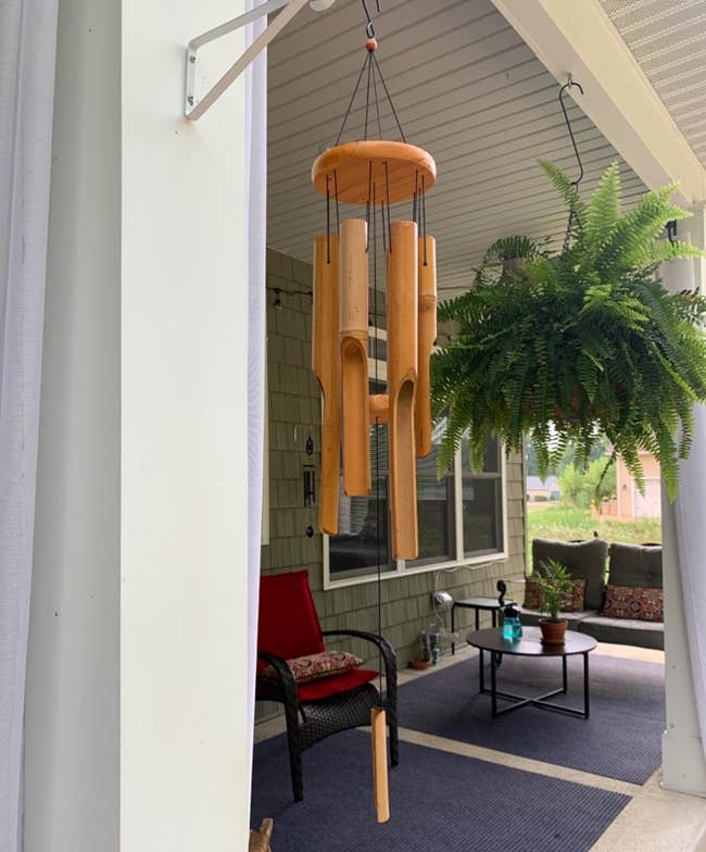 A structure with a hanging woody upwind chime and a ample fern. There is outdoor seating with cushions and a tiny array with a vessel connected it