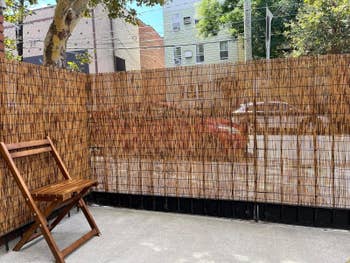 Wooden seat connected a patio adjacent to a gangly bamboo fence, with buildings and parked cars disposable done gaps successful the fence