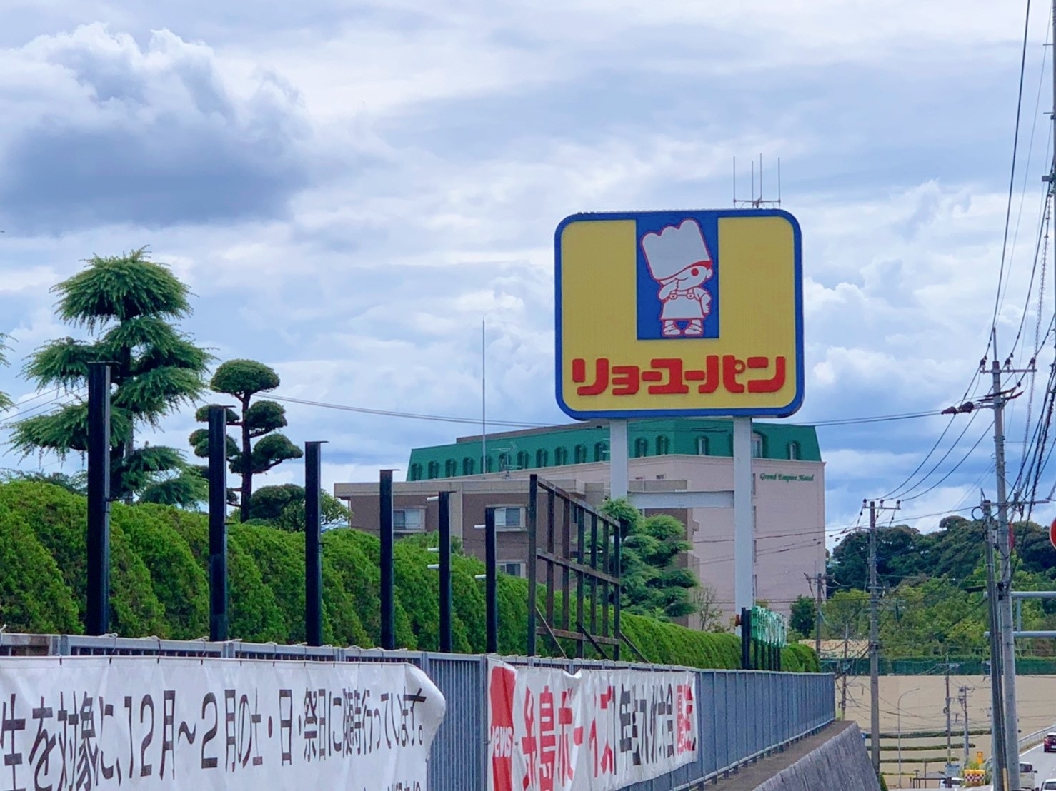 看板にパン職人のイラストと「リョーユーパン」と書かれている。背景に空と建物が見える。