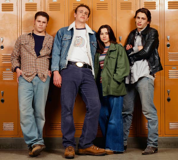 Seth Rogen as Ken Miller, Jason Segel as Nick Andopolis, Linda Cardellini as Lindsay Weir, and James Franco as Daniel Desario stand casually in front of lockers, dressed in 90s casual attire with jeans and jackets