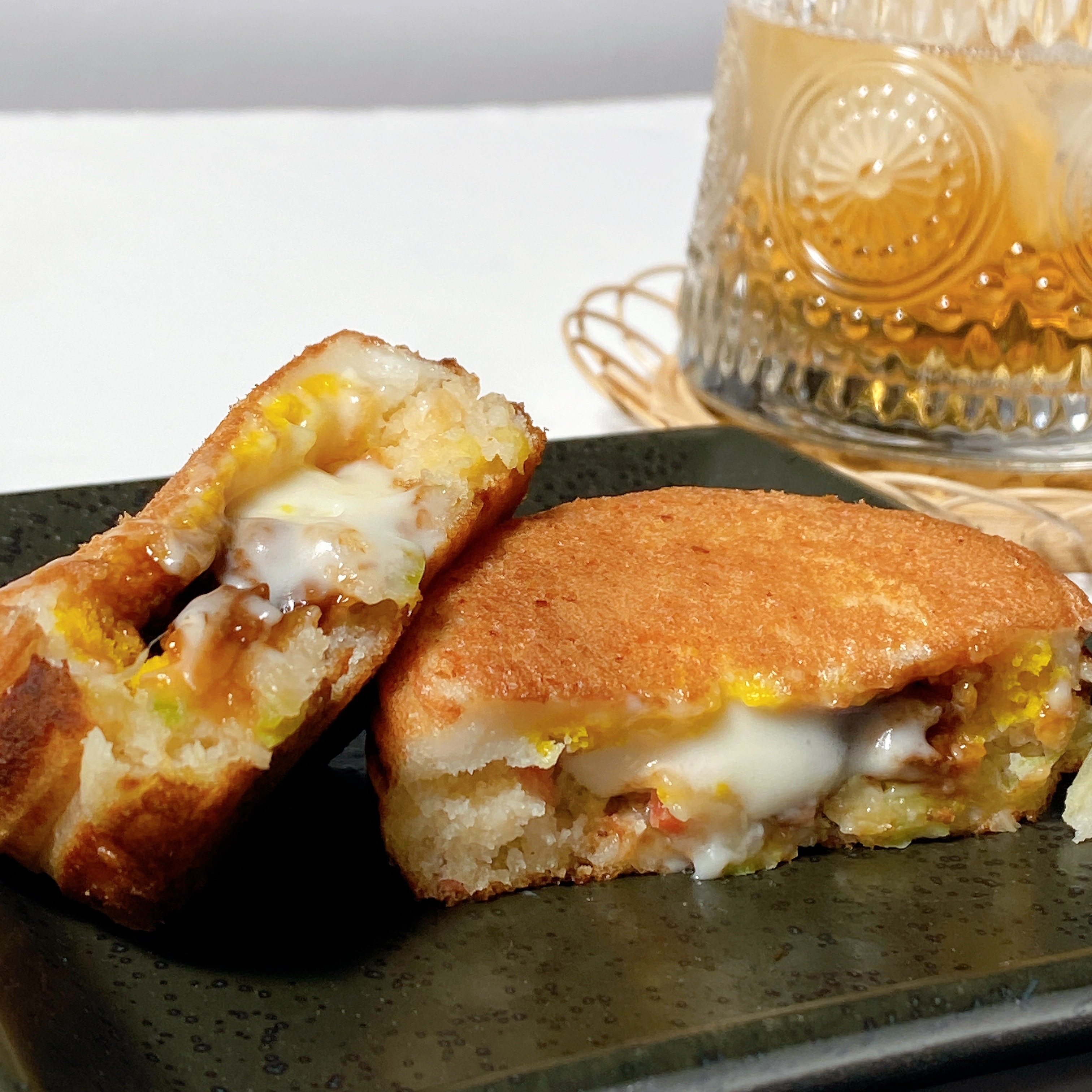 おいしそうなクリームチーズの詰まったドーナツが2つ、黒い皿に載っている。背景には模様の入ったグラス。