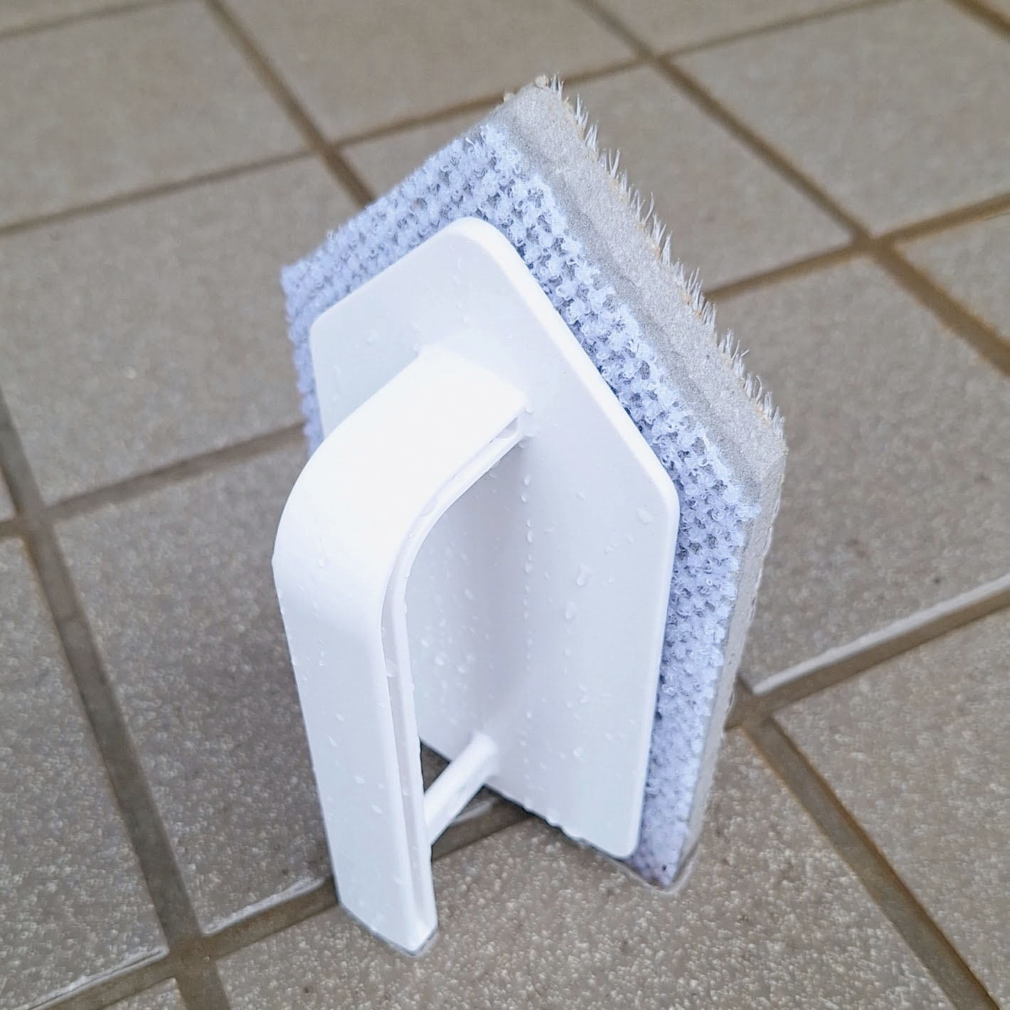 タイルの上に置かれたバス用スポンジブラシ。壁用の持ち手が付いています。