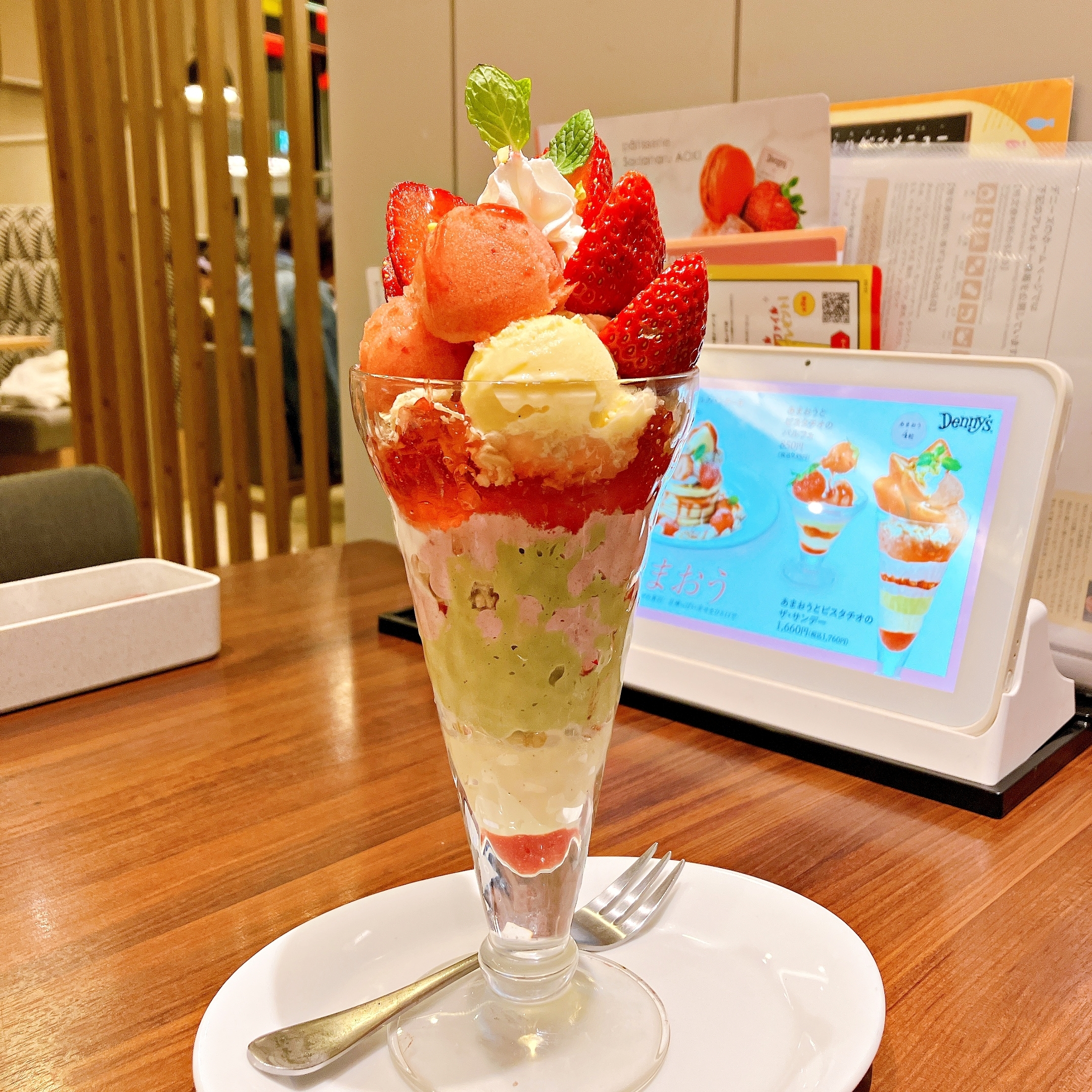 パフェの画像。いちごやアイスクリームがたっぷり乗り、豪華なデザート。背景にメニューが写っている。