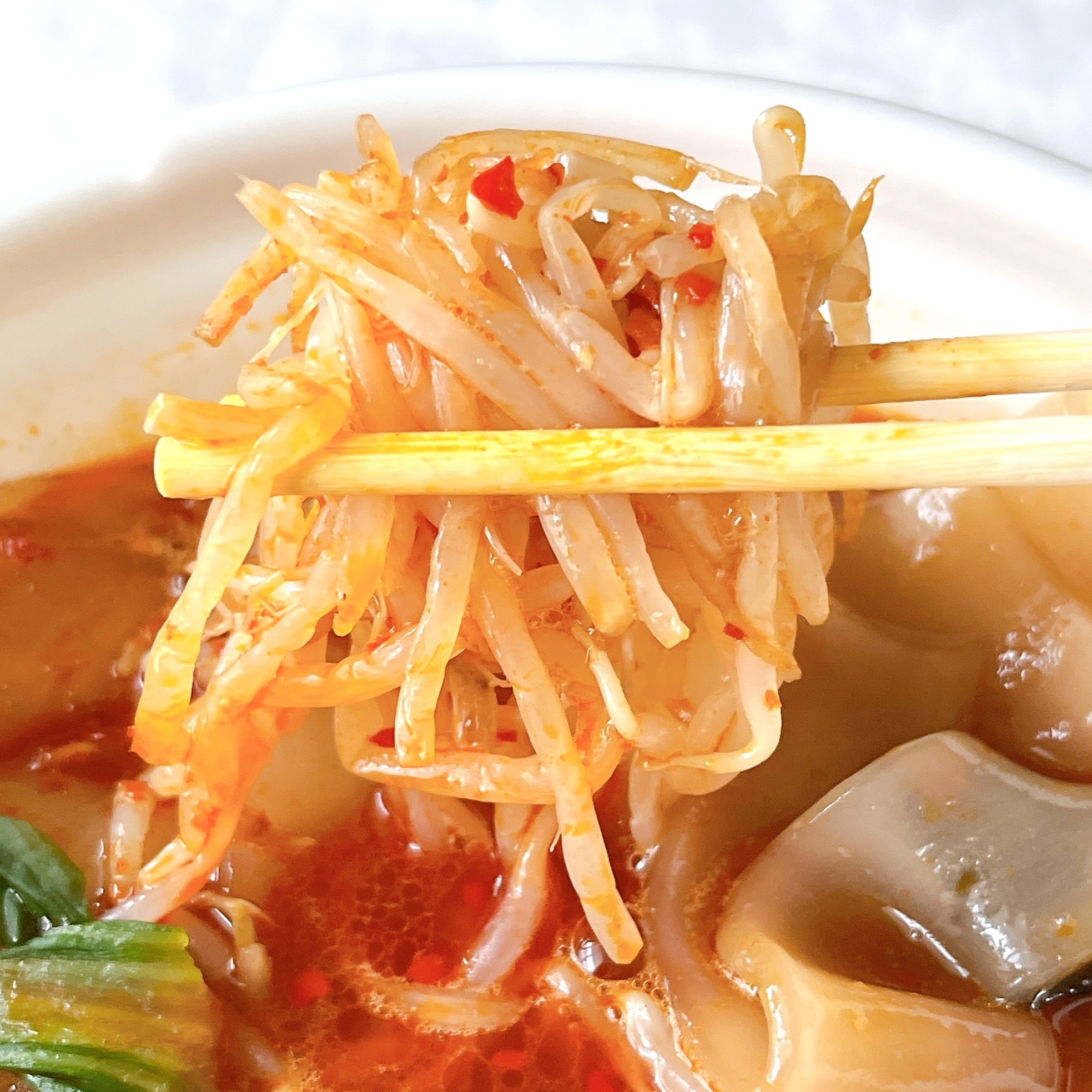 ラーメンの器から箸で持ち上げられたもやしとスープの一部。