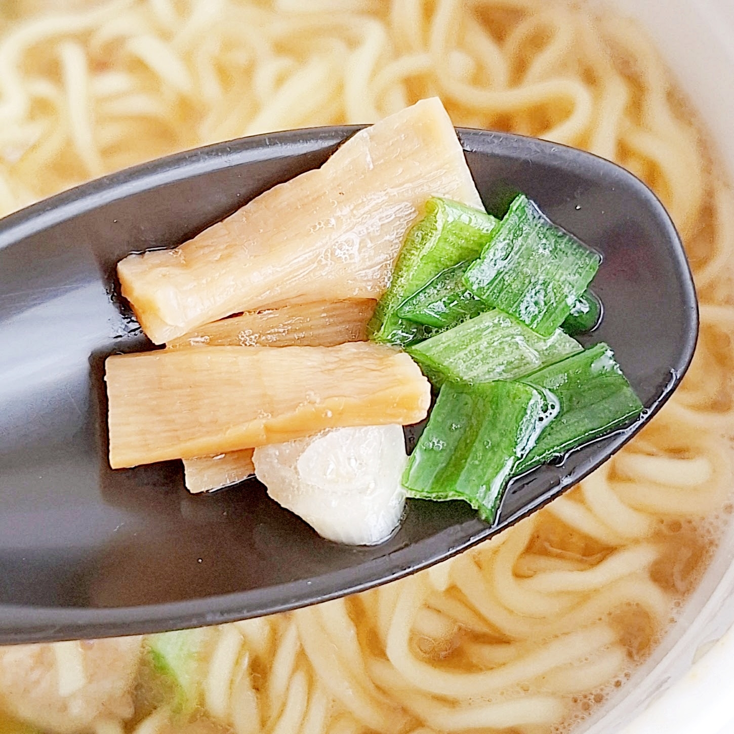黒いスプーンに載ったメンマ、ネギ、ニンニクとラーメン。