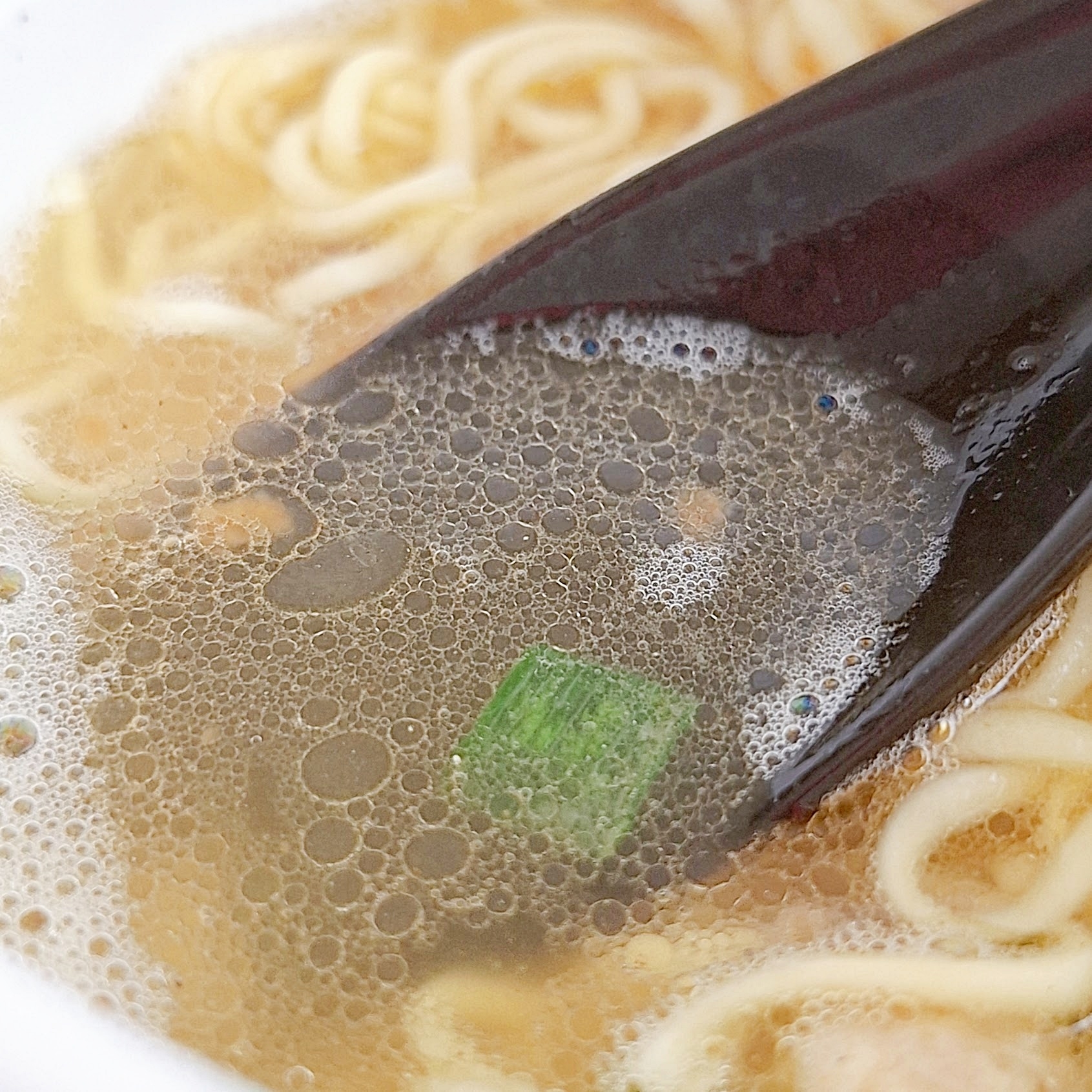 ラーメンのスープに浮かぶ具材と上に置かれたレンゲ。