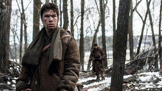 Character in rugged, medieval-style clothing stands in a snowy forest, looking concerned; another figure is blurred in the background