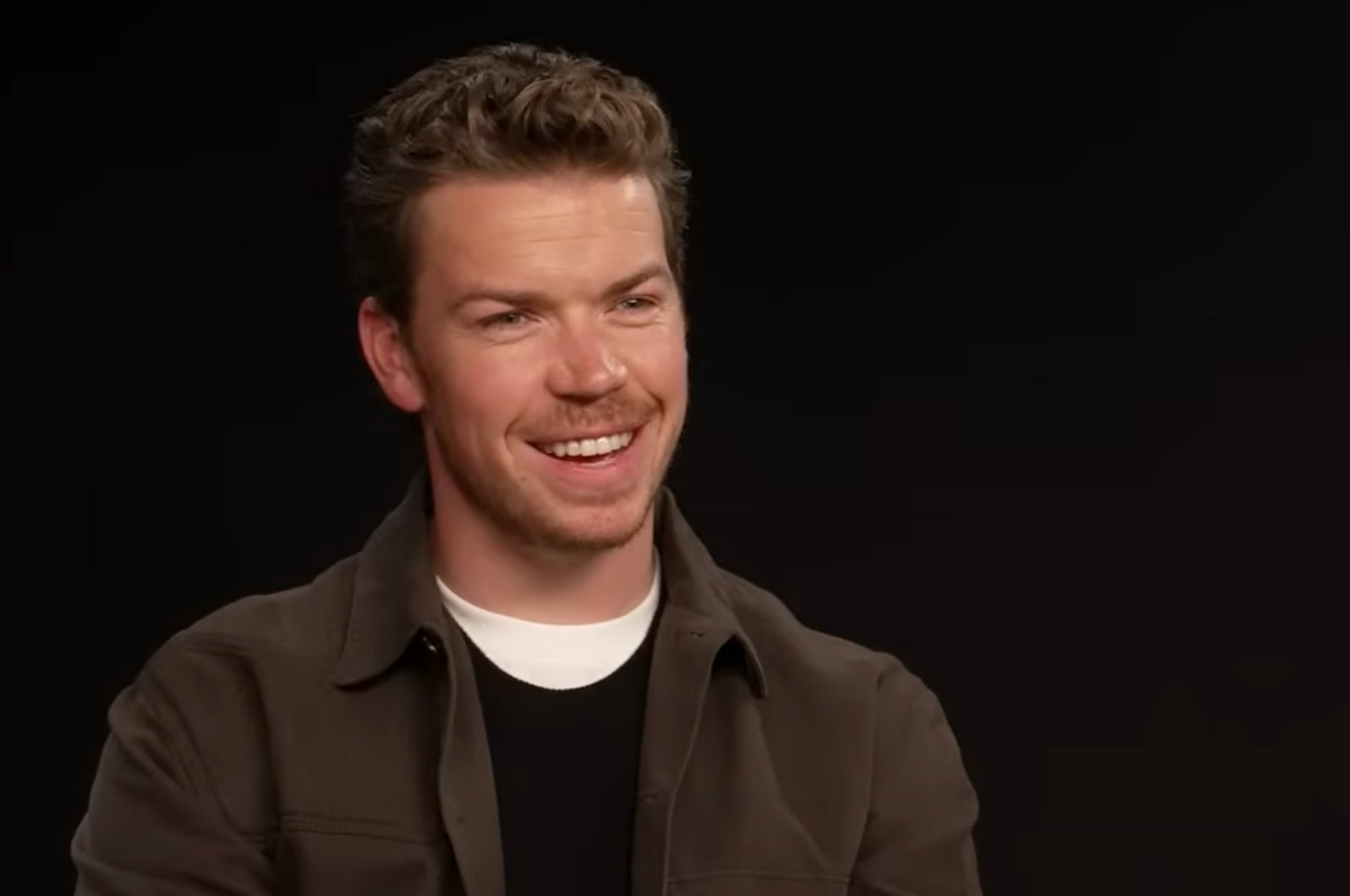 Person smiling and wearing a casual jacket over a shirt, in an interview setting