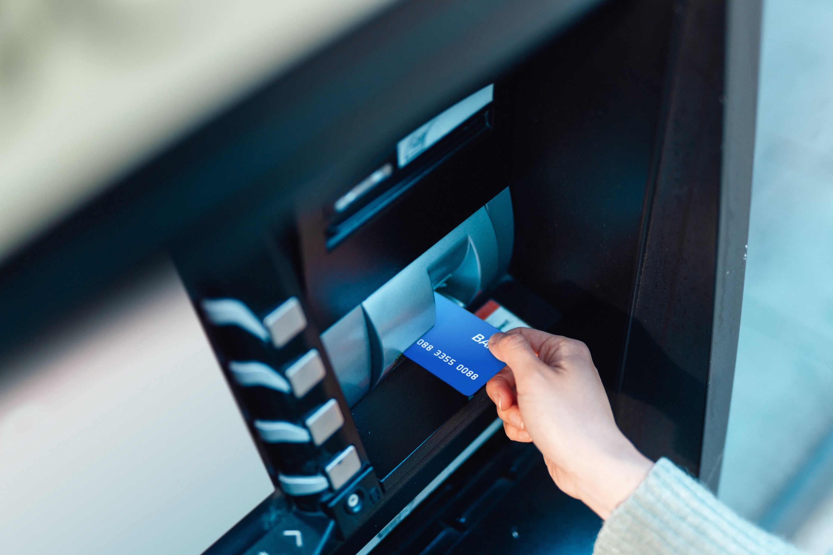 Person inserting a bank card into an ATM machine, focusing on financial transactions and access to funds
