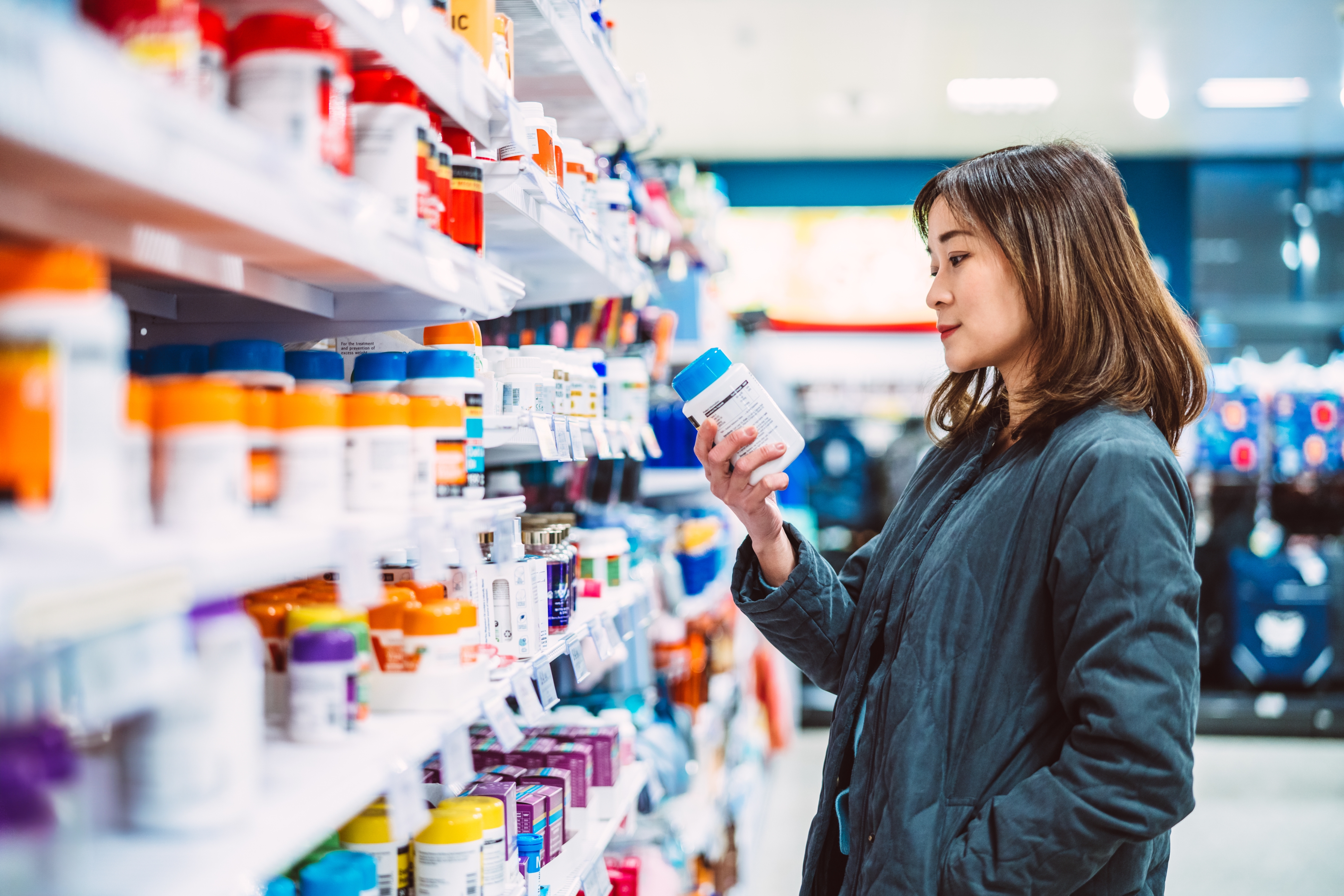 Person in a store aisle examining a bottle, surrounded by various products on shelves
