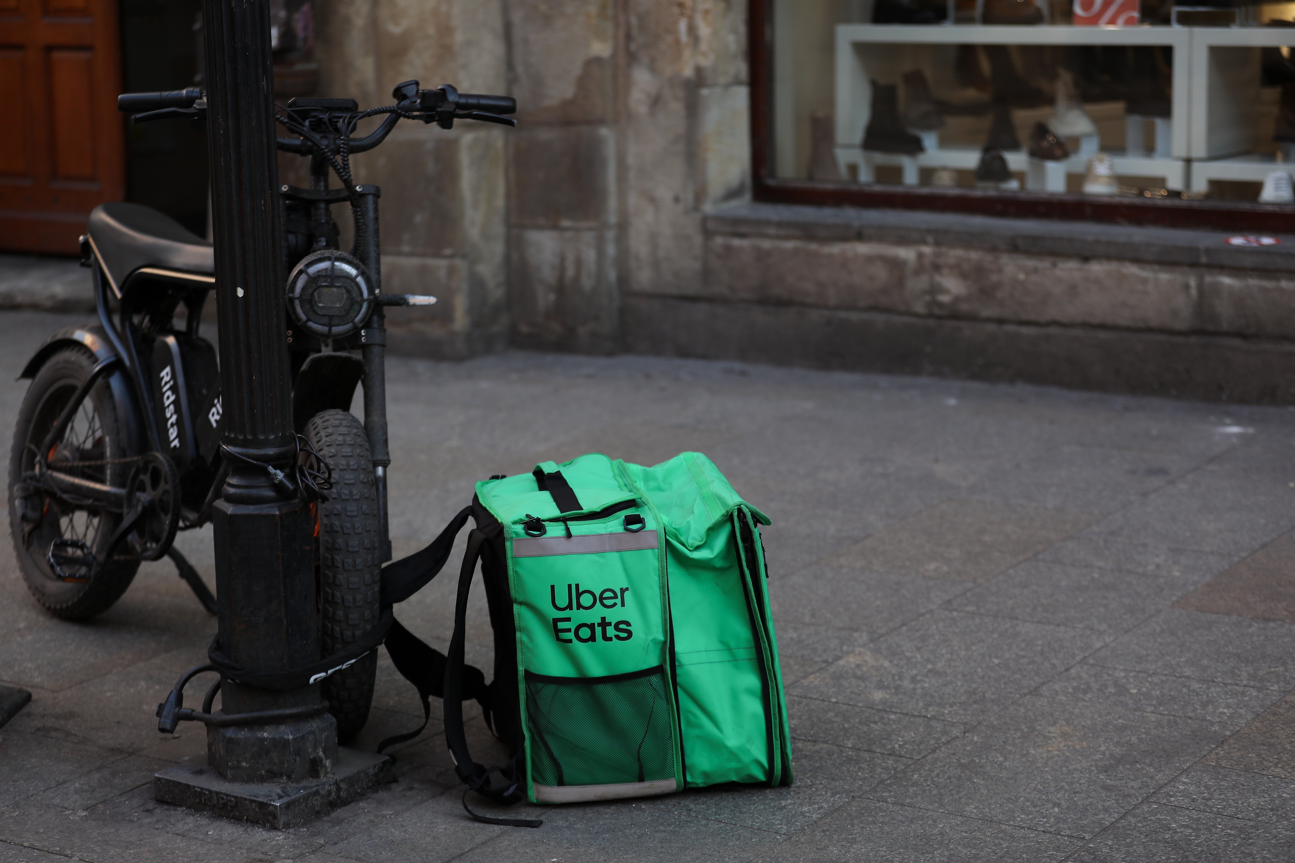 Uber Eats delivery bag on sidewalk next to a motorbike, outside a shop window