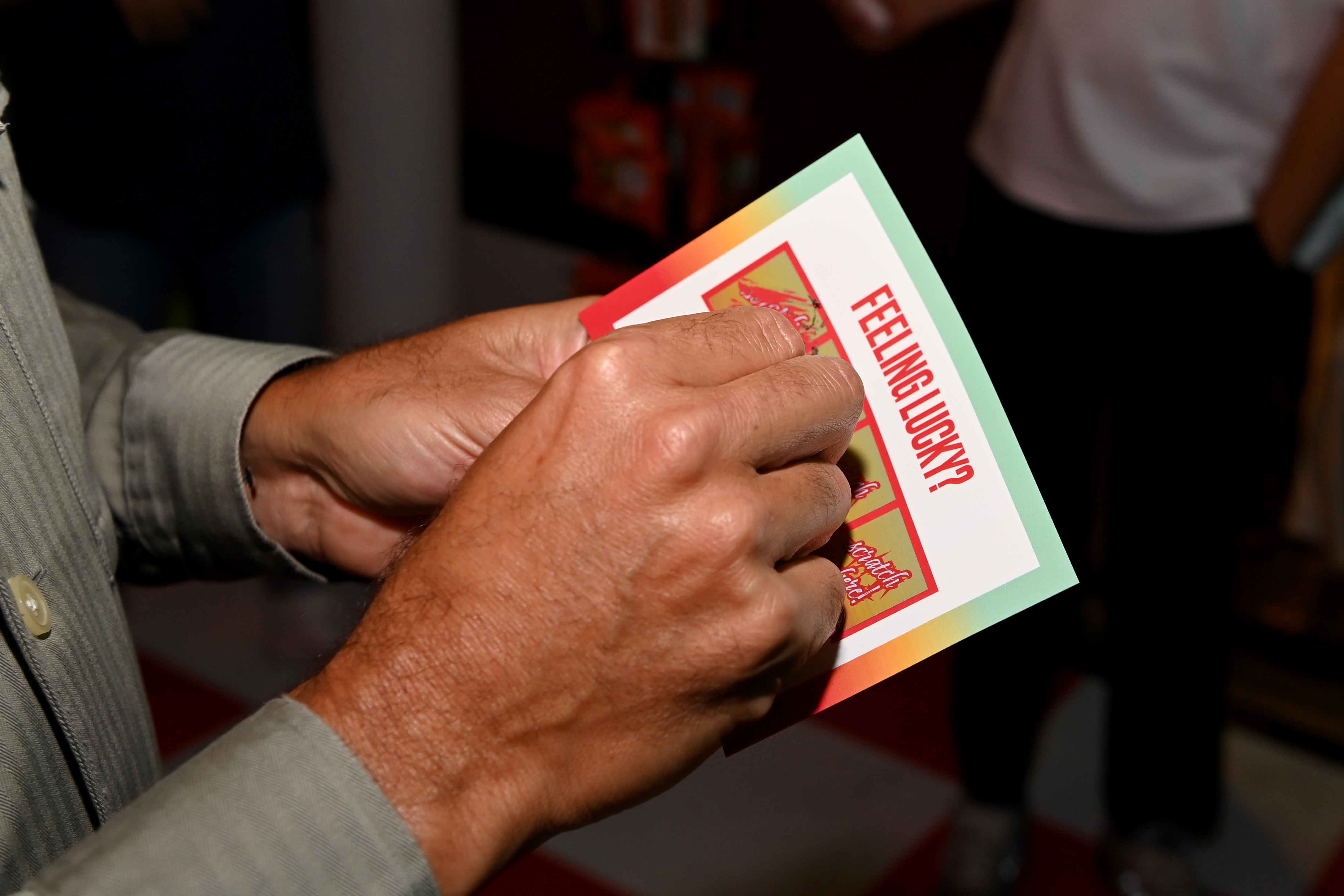 Person holding scratch-off lottery ticket with the phrase "FEELING LUCKY?" visible on the card