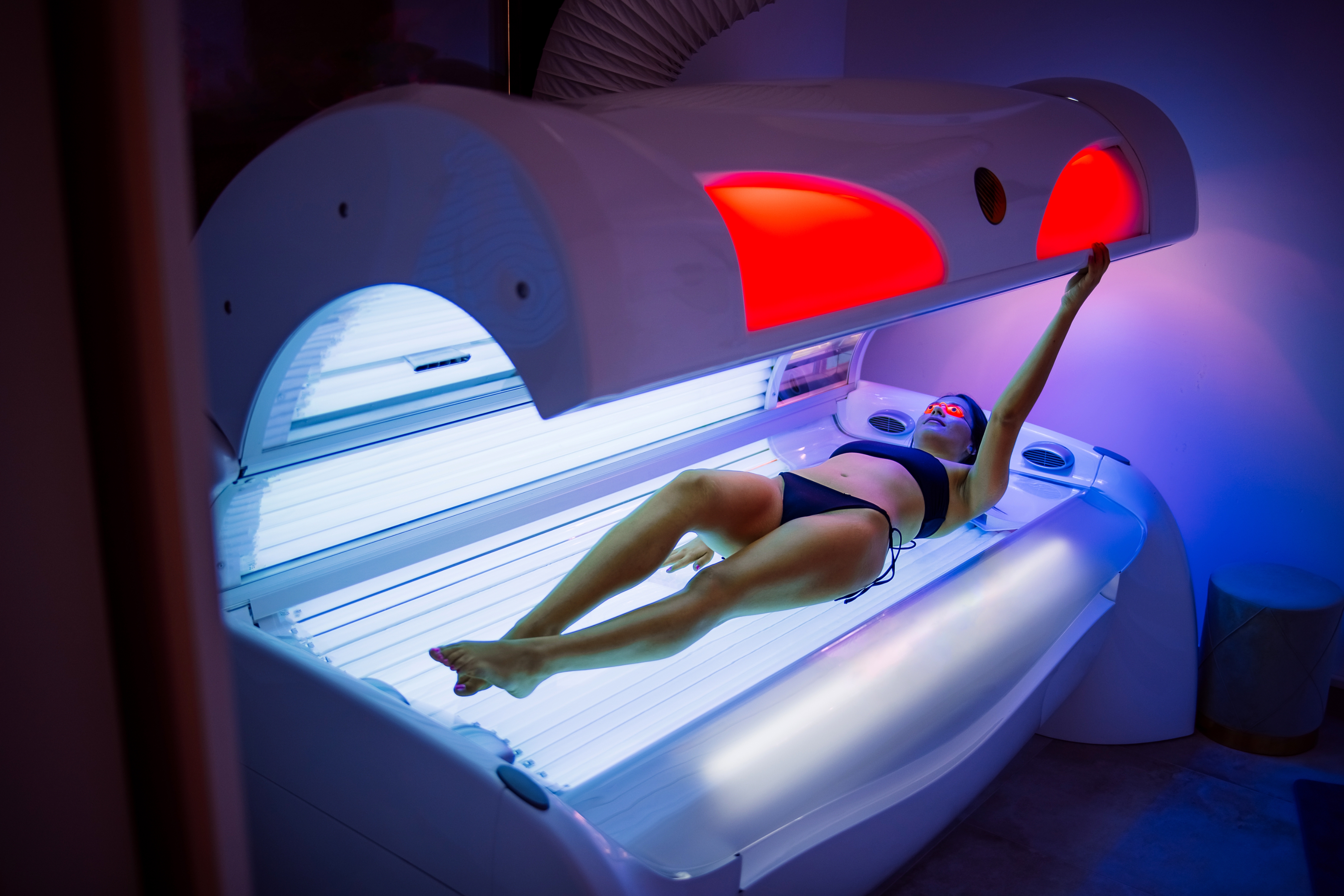 Person in a tanning bed, reaching up to touch the lid. Article relates to workplace or financial aspects of tanning salons