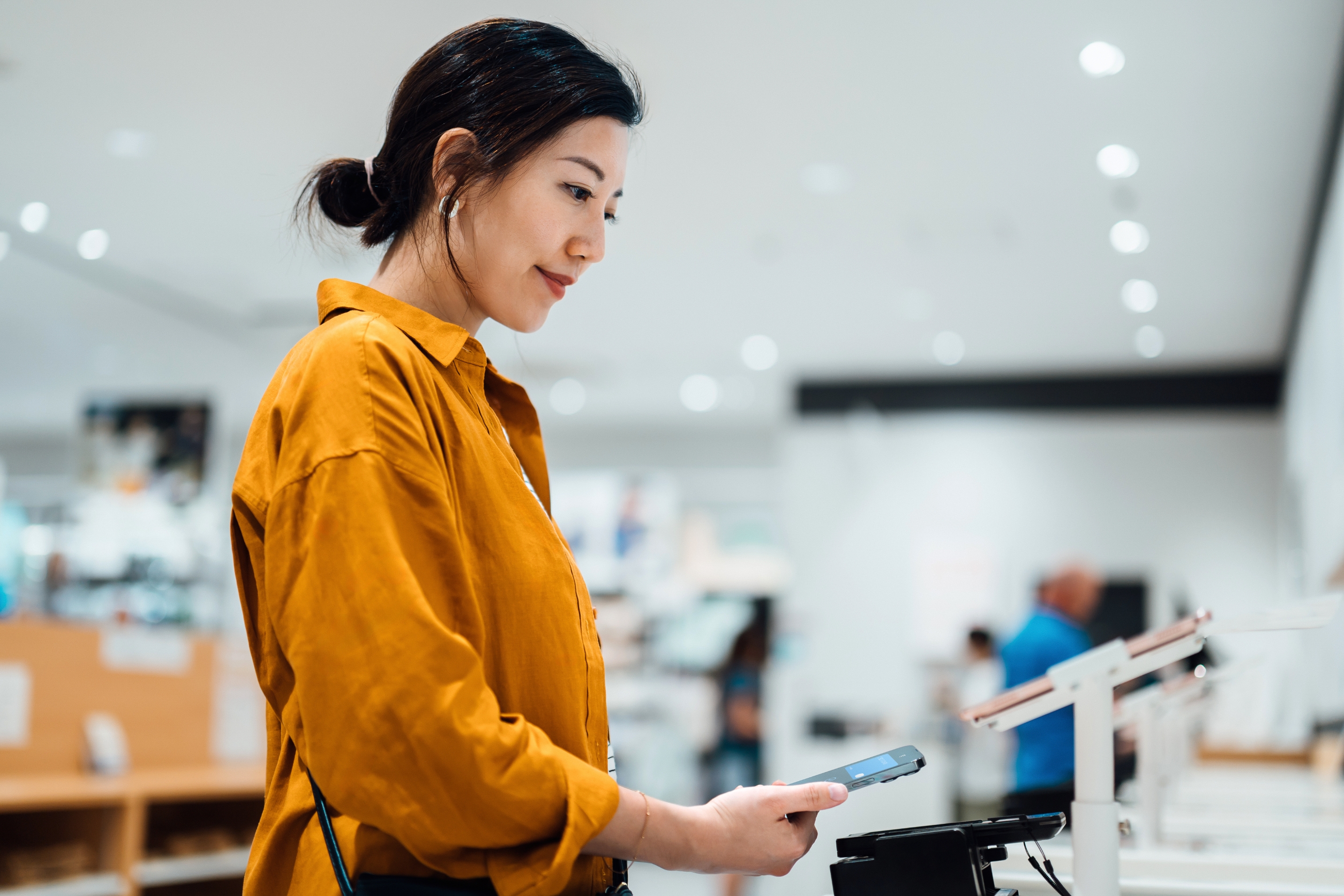 Person in a store making a purchase with a smartphone at a digital payment terminal, wearing a stylish, relaxed outfit