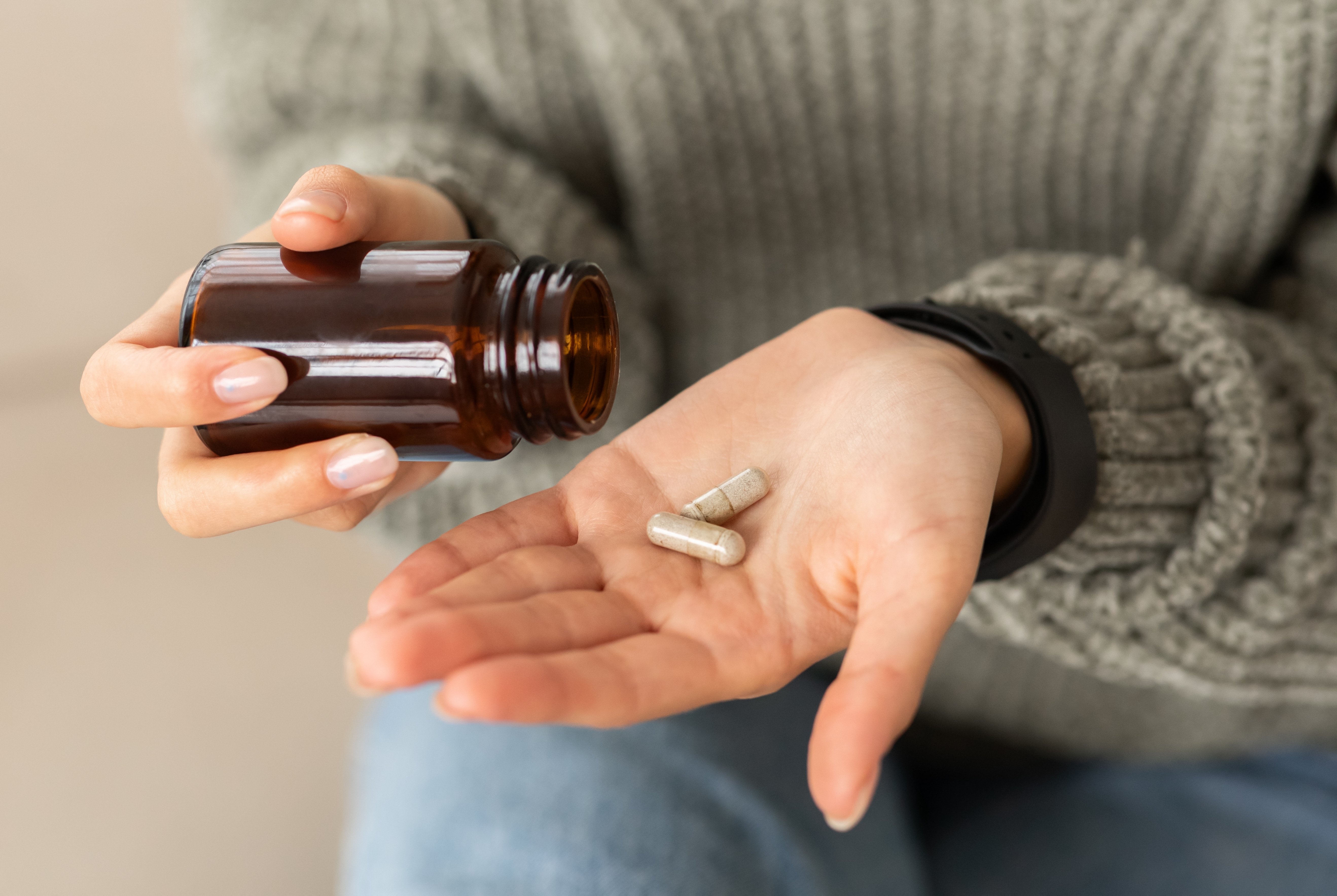 A person holds an open pill bottle in one hand and two capsules in the other, suggesting health or wellness context
