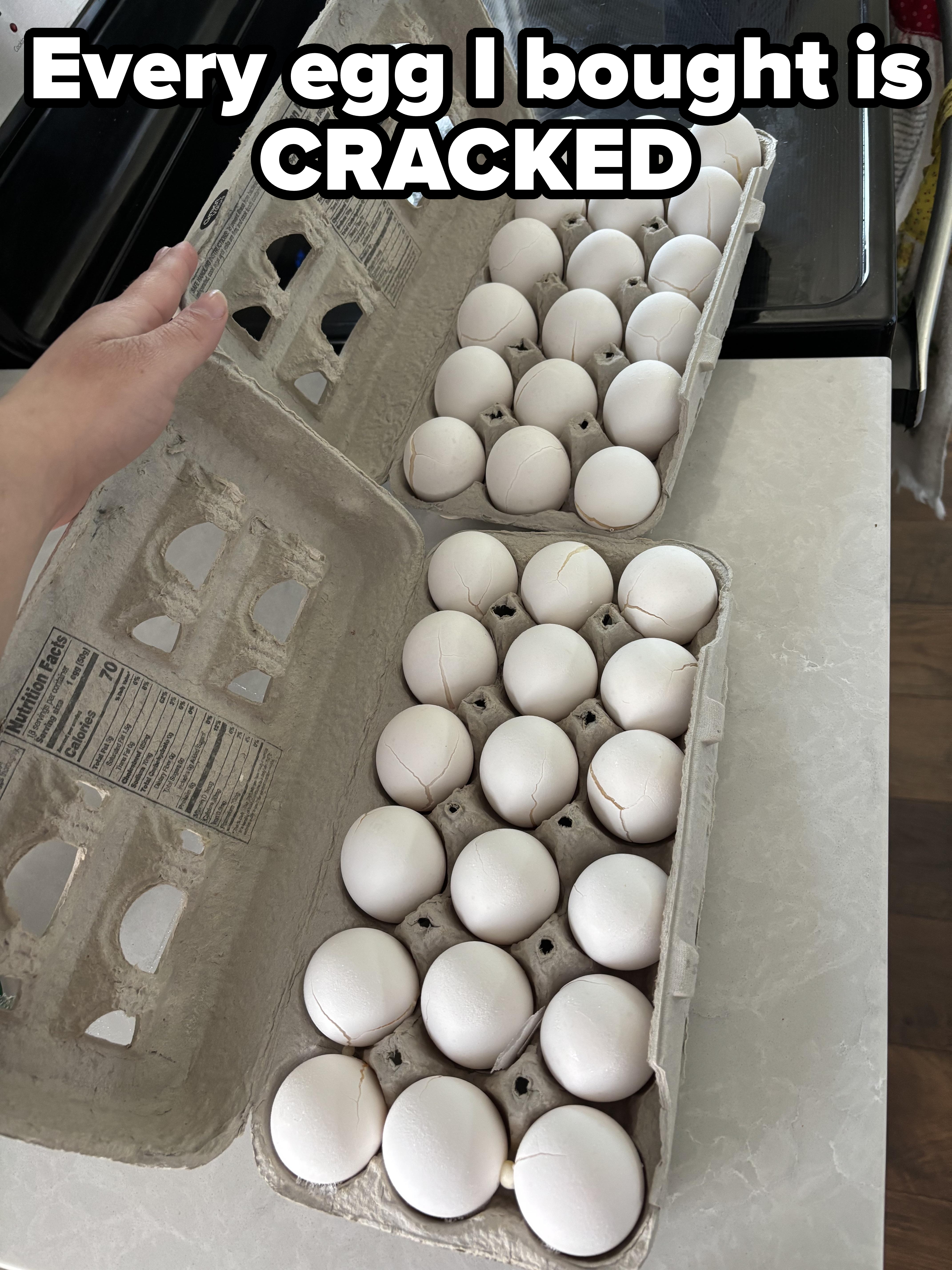 Carton of eggs is placed on a counter, some cracked. A hand lifts the lid of another carton