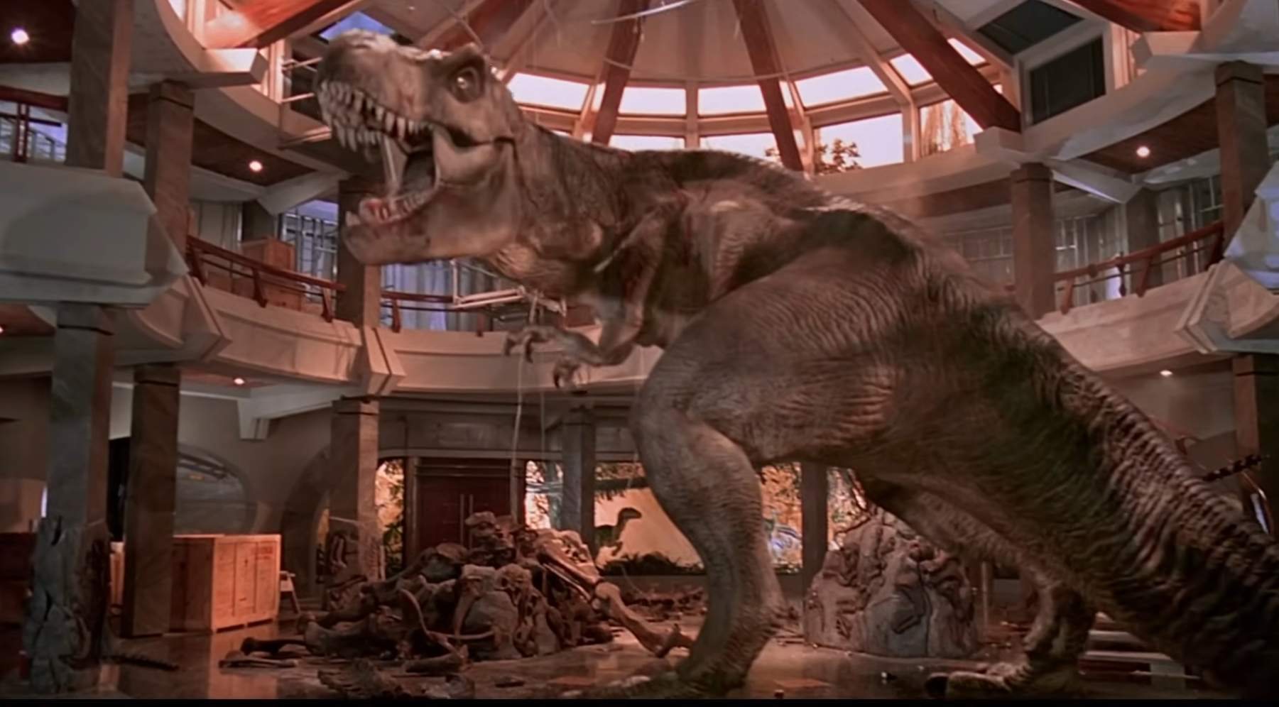 A T-Rex roars inside a museum-like building, with sculptures and debris surrounding it