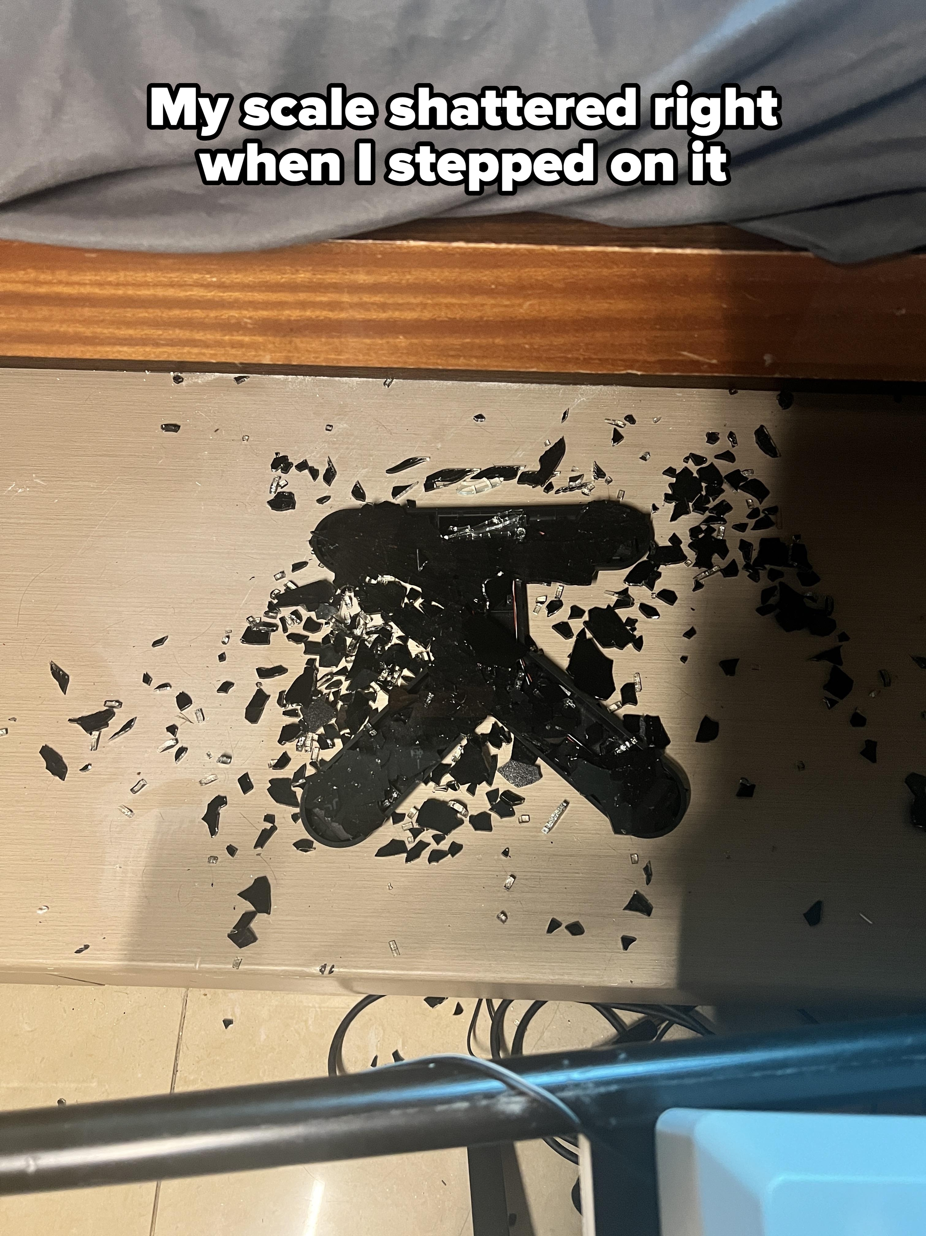 Shattered TV remote with black fragments scattered on the floor, near a piece of furniture