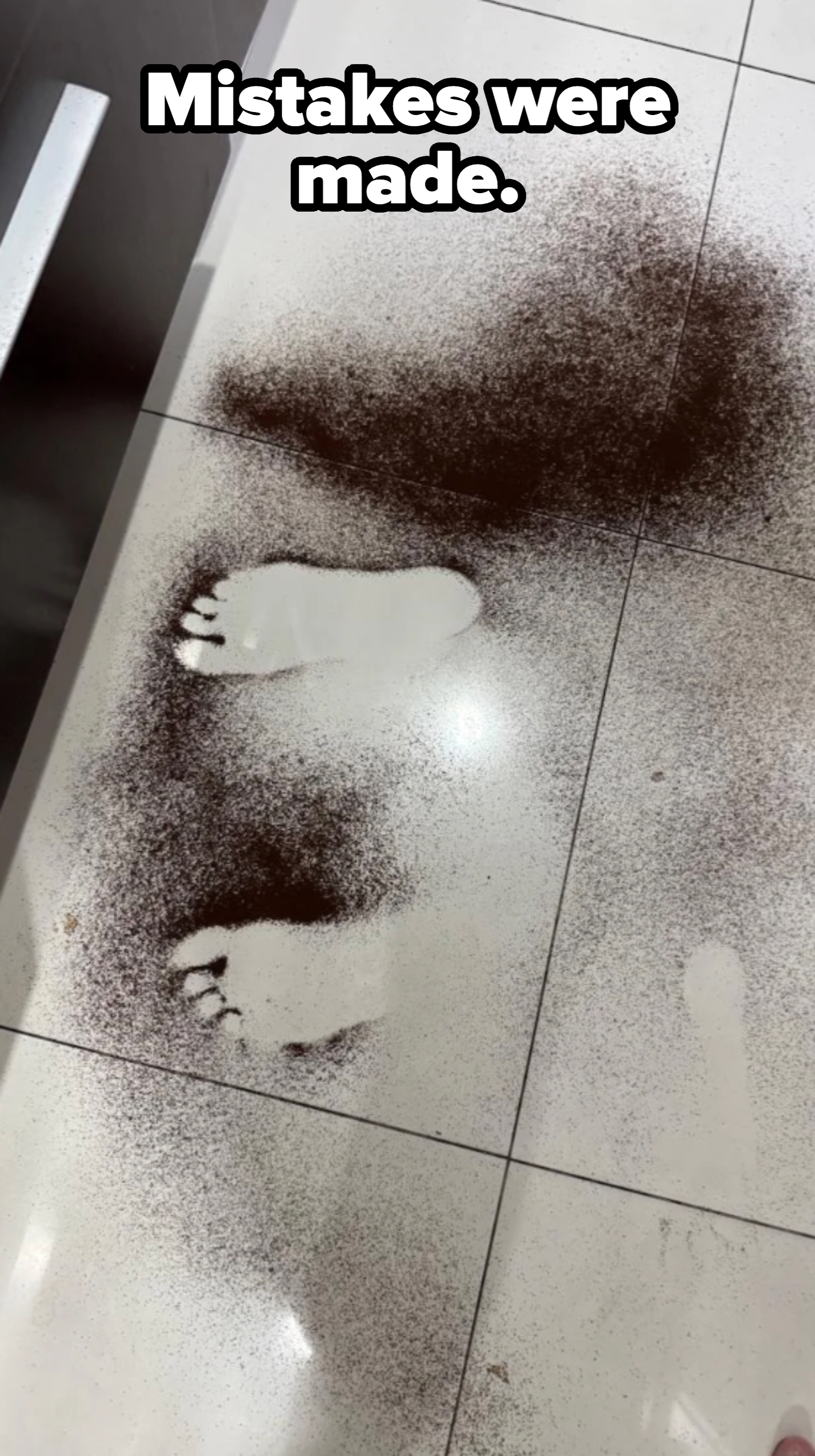 Two footprints on a white tiled floor surrounded by scattered coffee grounds
