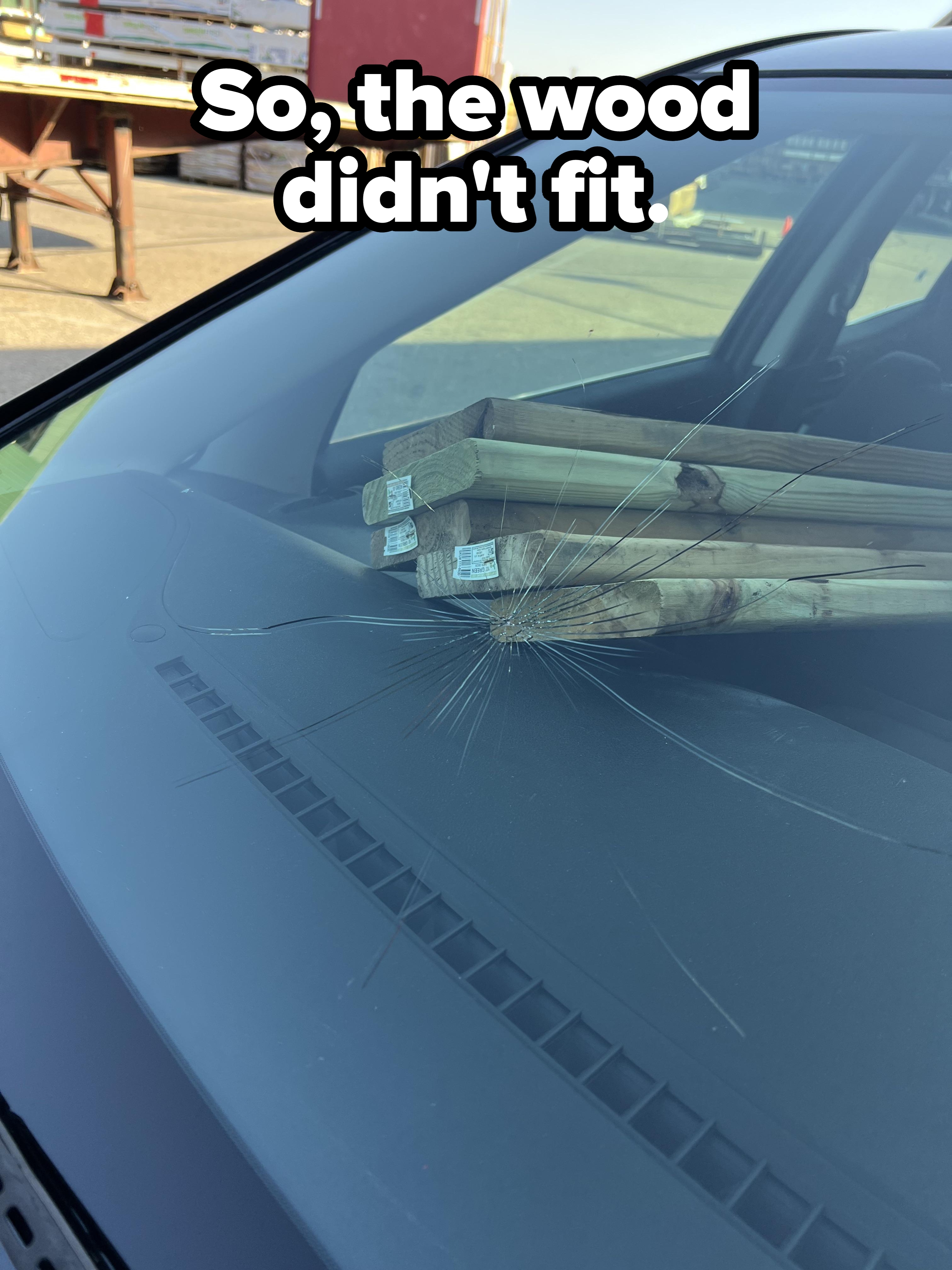 Wooden beams pierce a car windshield, showing visible cracks. The beams extend into the car's interior. Scene suggests a road incident