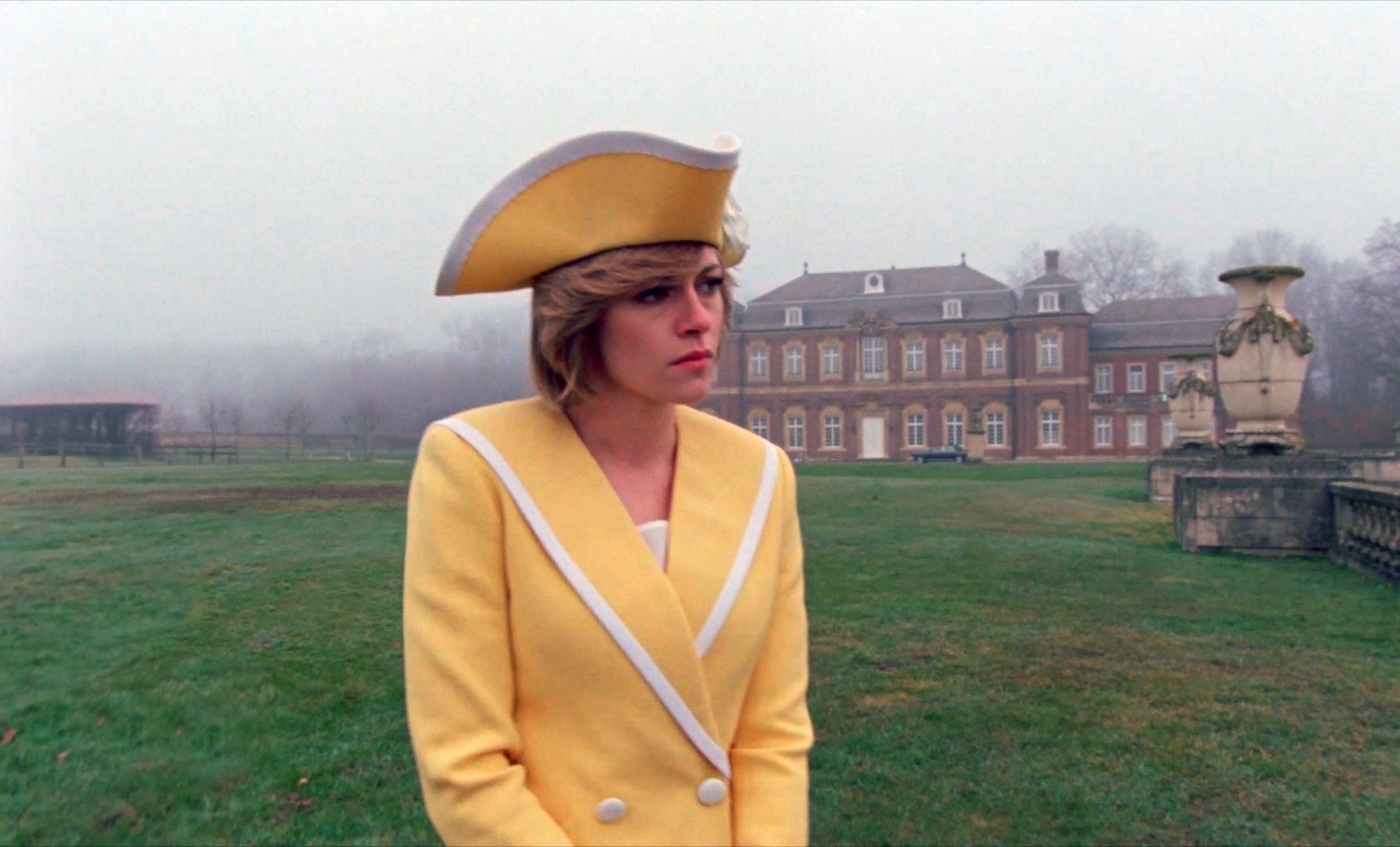 Kristen Stewart as Princess Diana in "Spencer" outside a large building in the fog