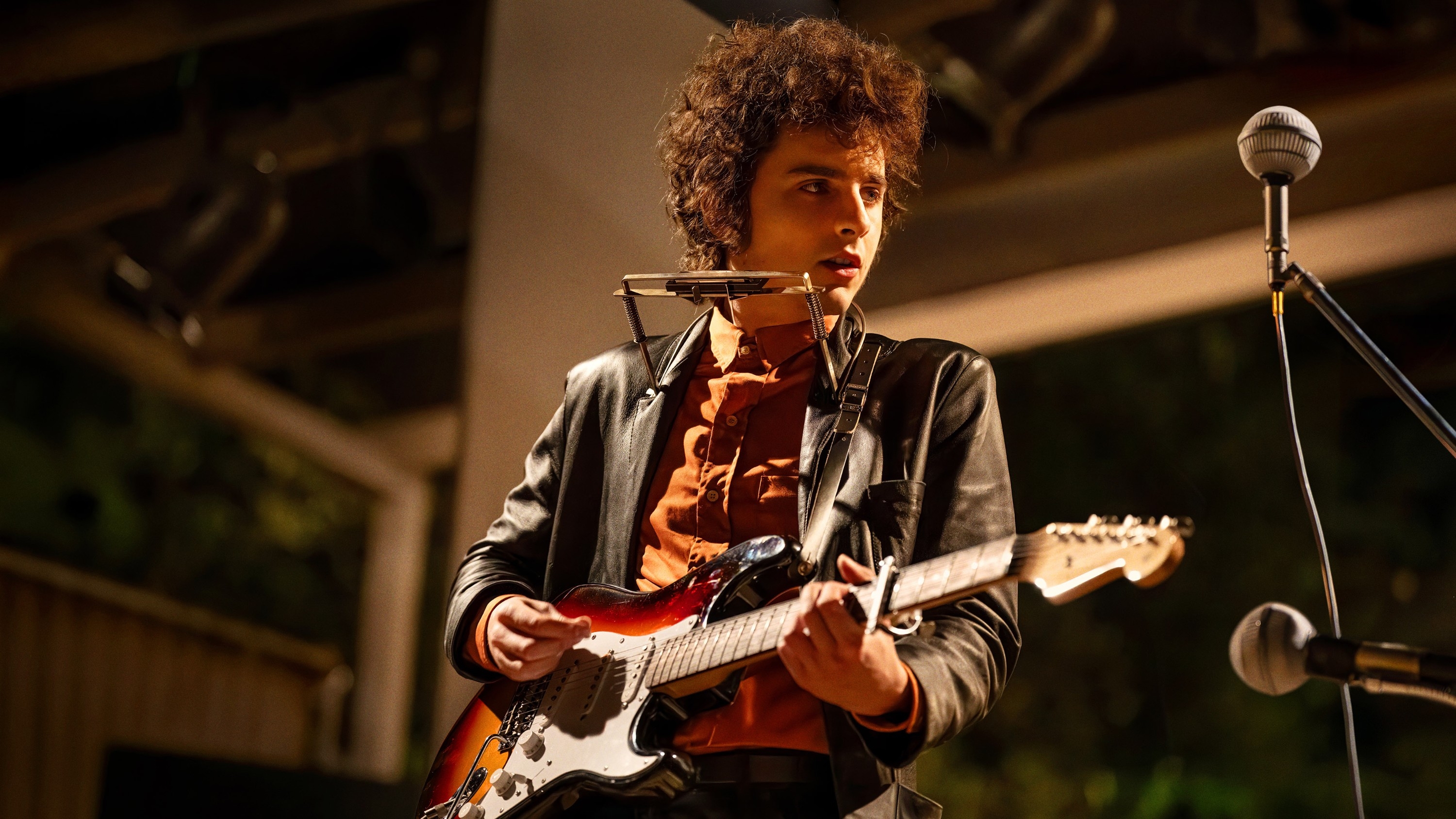 Timothée Chalamet as Bob Dylan in "A Complete Unknown" playing the guitar and harmonica onstage