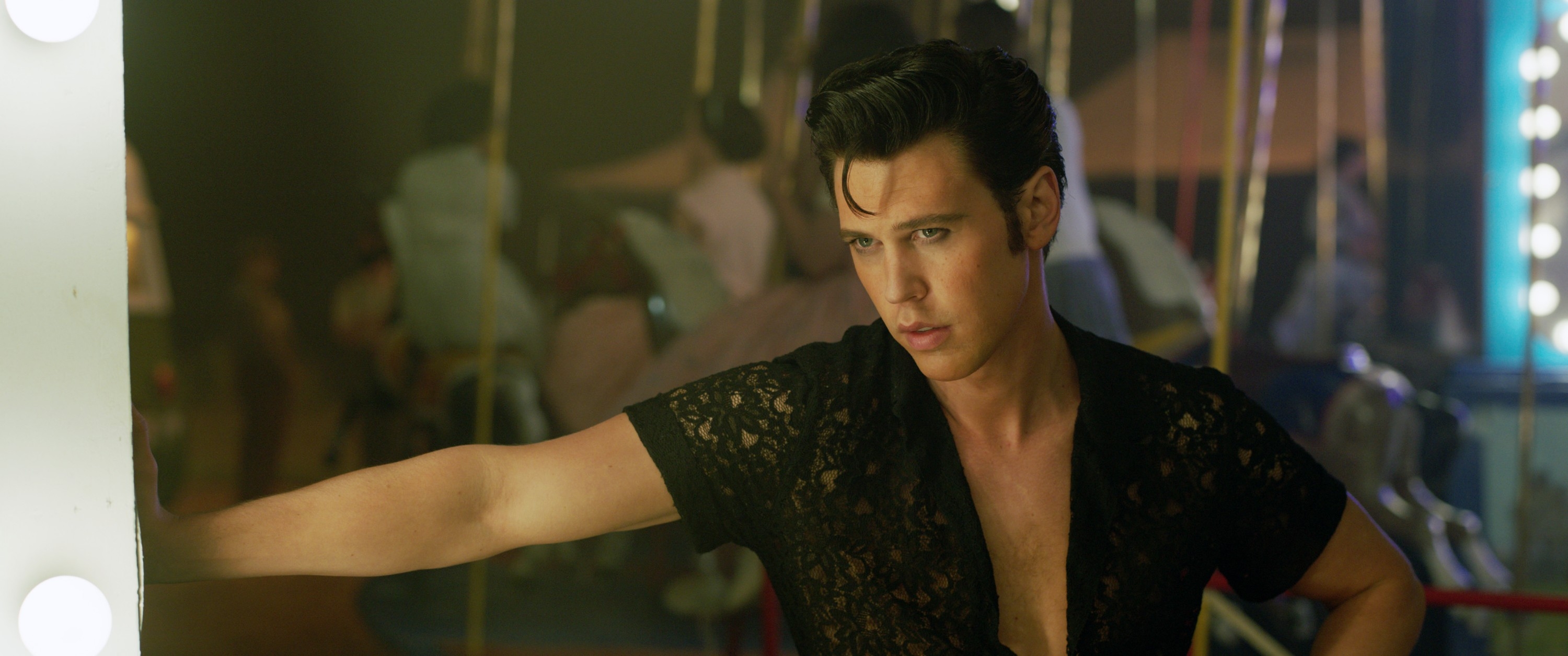 Austin Butler as Elvis Presley in "Elvis" in a lace shirt leaning his hand against a wall