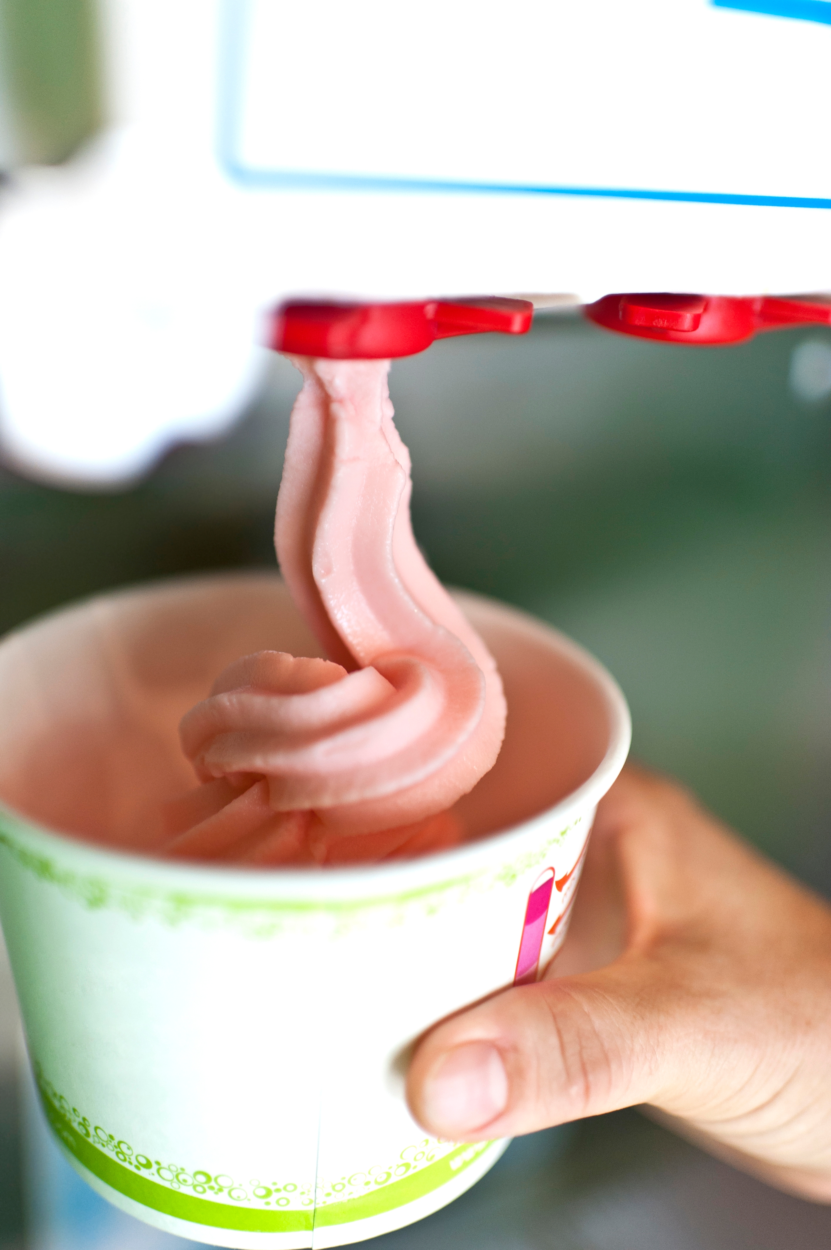 Soft serve ice cream being dispensed into a paper cup held by a hand