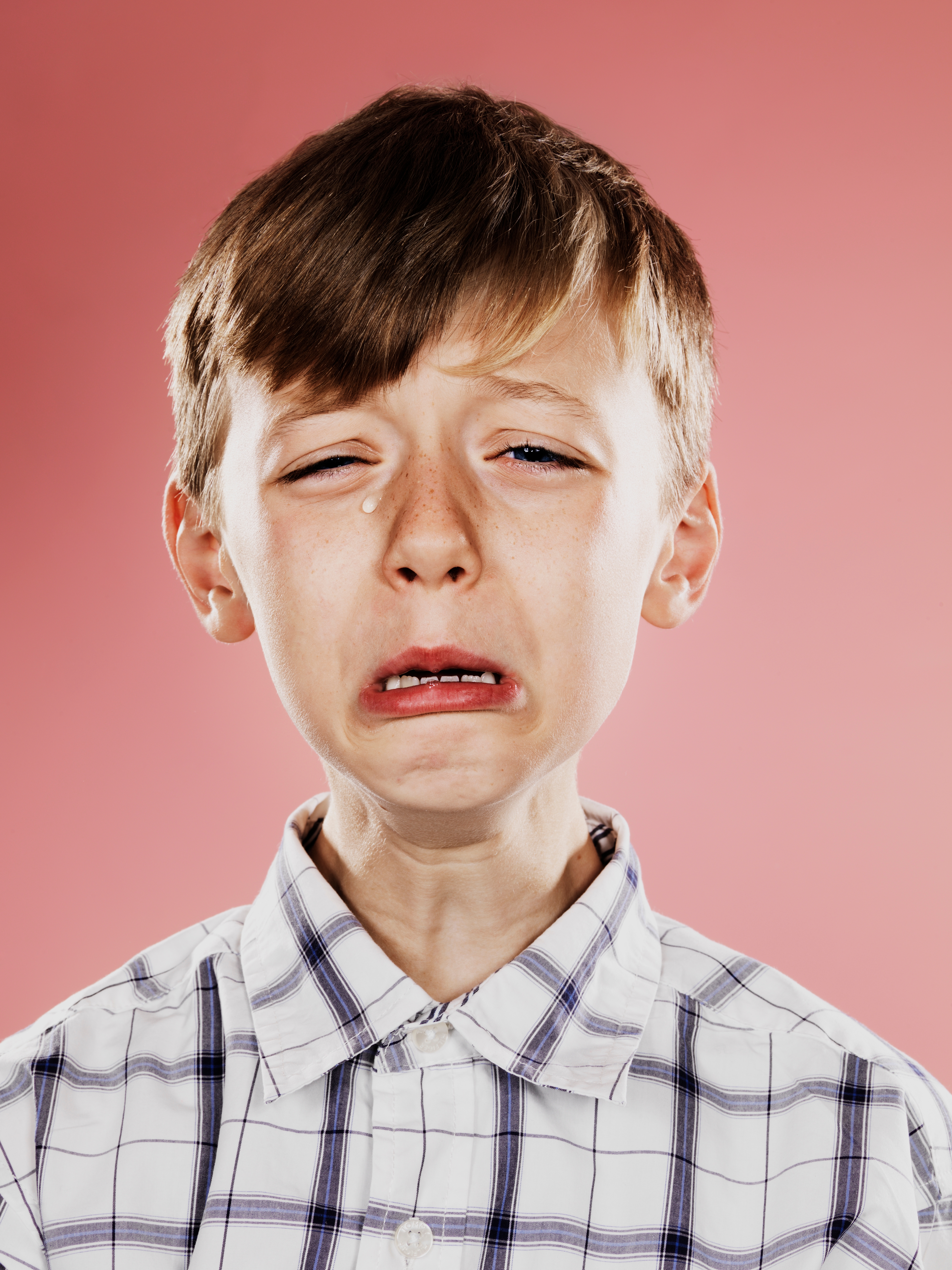 Child crying, wearing a plaid shirt, with a tear running down his cheek against a plain background