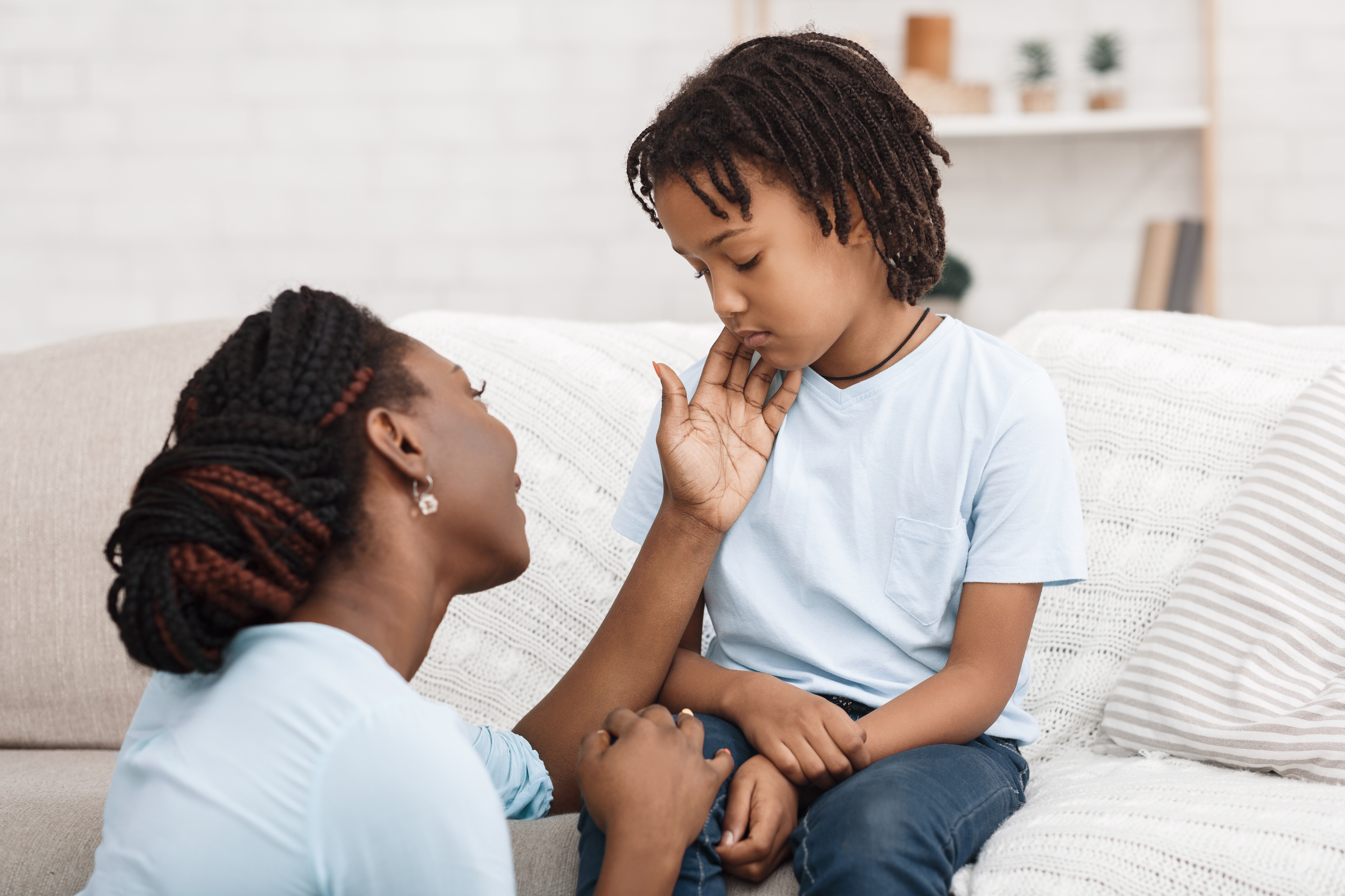 A parent gently comforts a child sitting on a couch, holding their hand and reassuring them