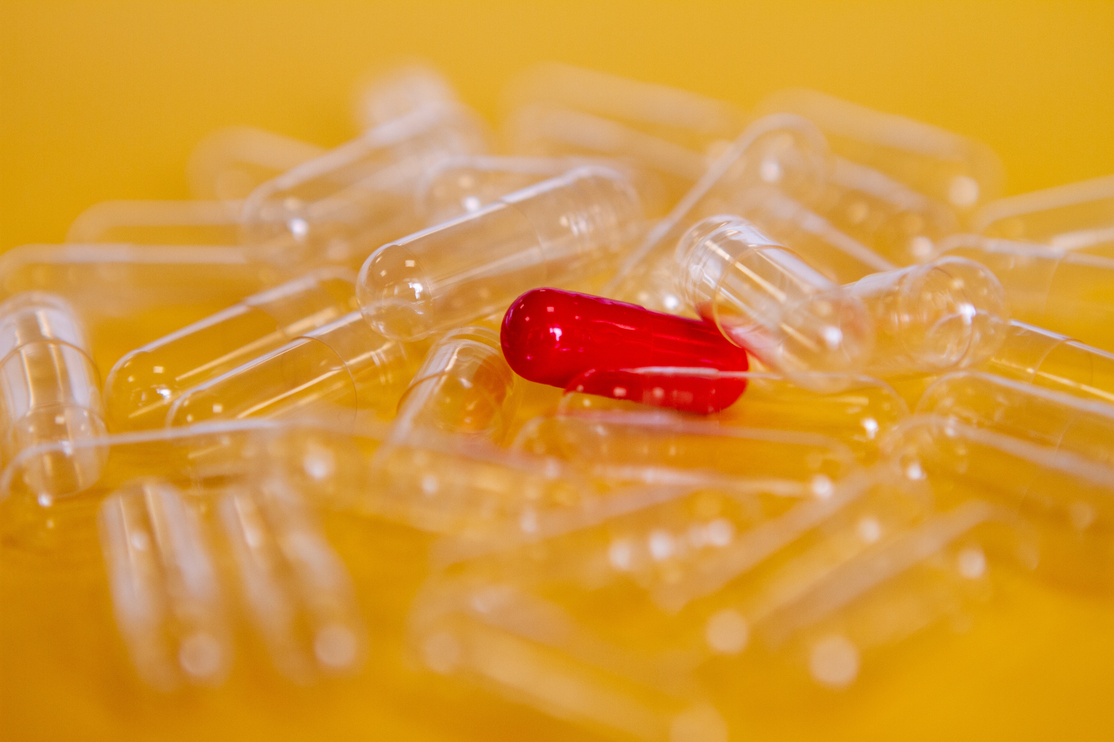 Red pill surrounded by empty clear capsules on a solid background