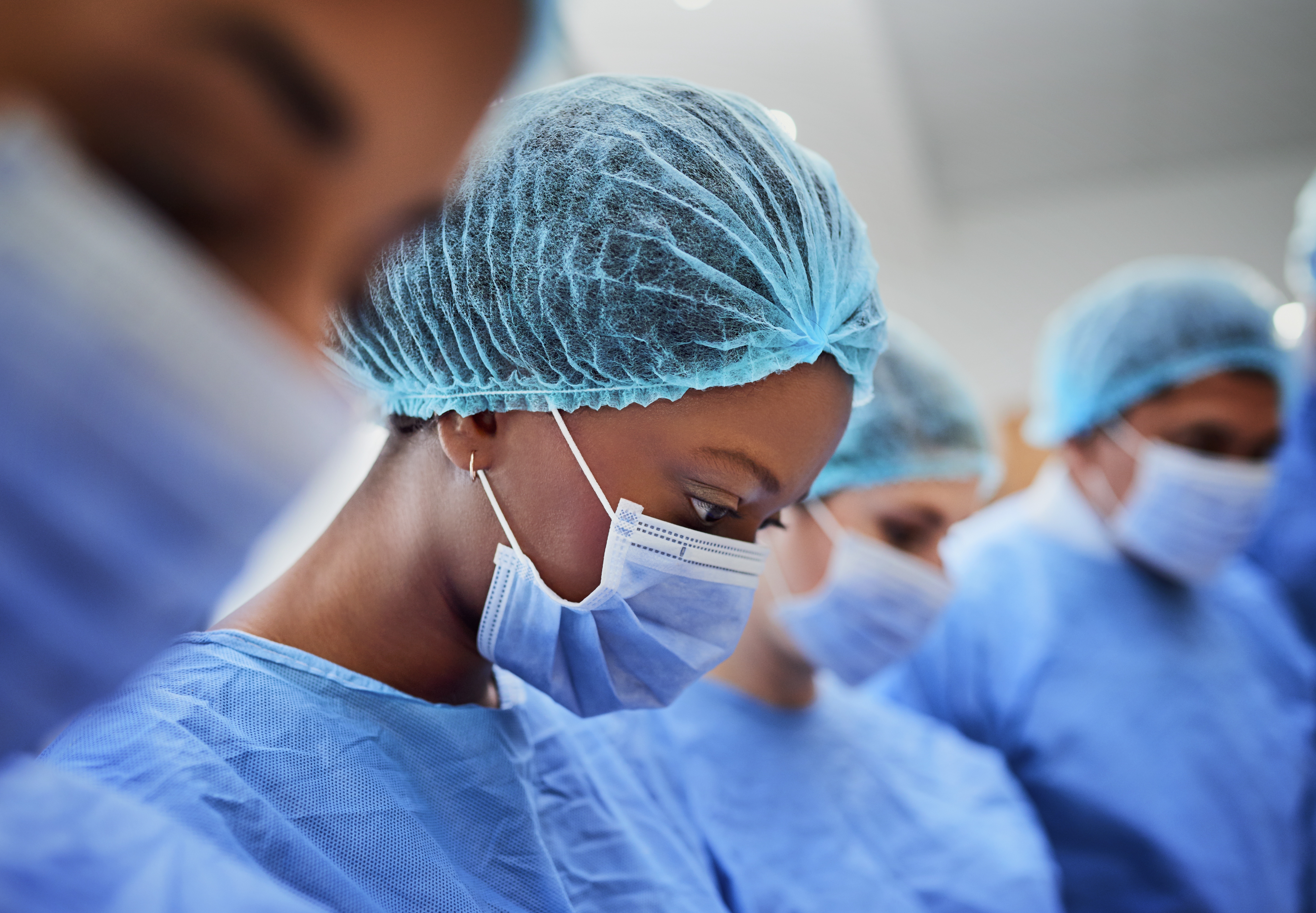 Medical professionals wearing surgical gowns, masks, and caps focus intently, suggesting a scene in a surgical or sterile environment