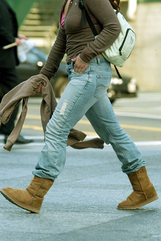 Person walking on a city street wearing casual jeans, UGG-style boots, and carrying a backpack
