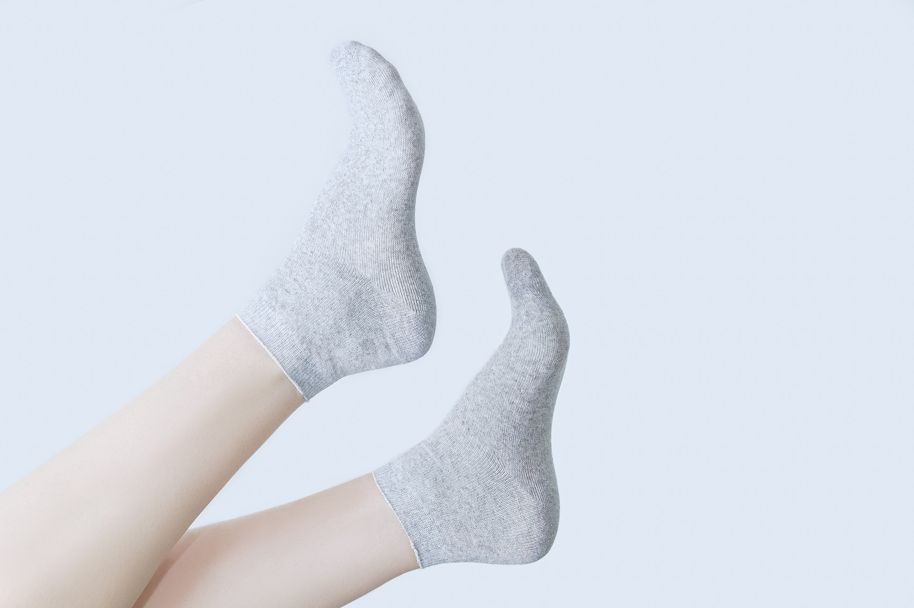Two feet wearing simple socks are playfully raised in the air against a plain background