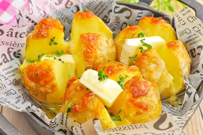 鉄のフライパンに入った焼きポテト。溶けたチーズとバターがトッピングされ、パセリが飾られている。新聞紙が敷かれている。