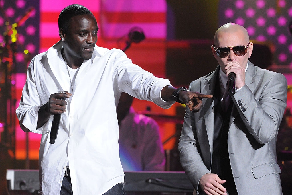 Two performers on stage: one in a white shirt, singing and pointing, the other in a gray suit with sunglasses, holding a microphone
