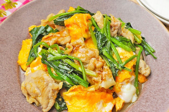 お皿に盛られた中華風の炒め物。肉、卵、緑の葉野菜が混ざっている。背景にテーブルクロスが見える。