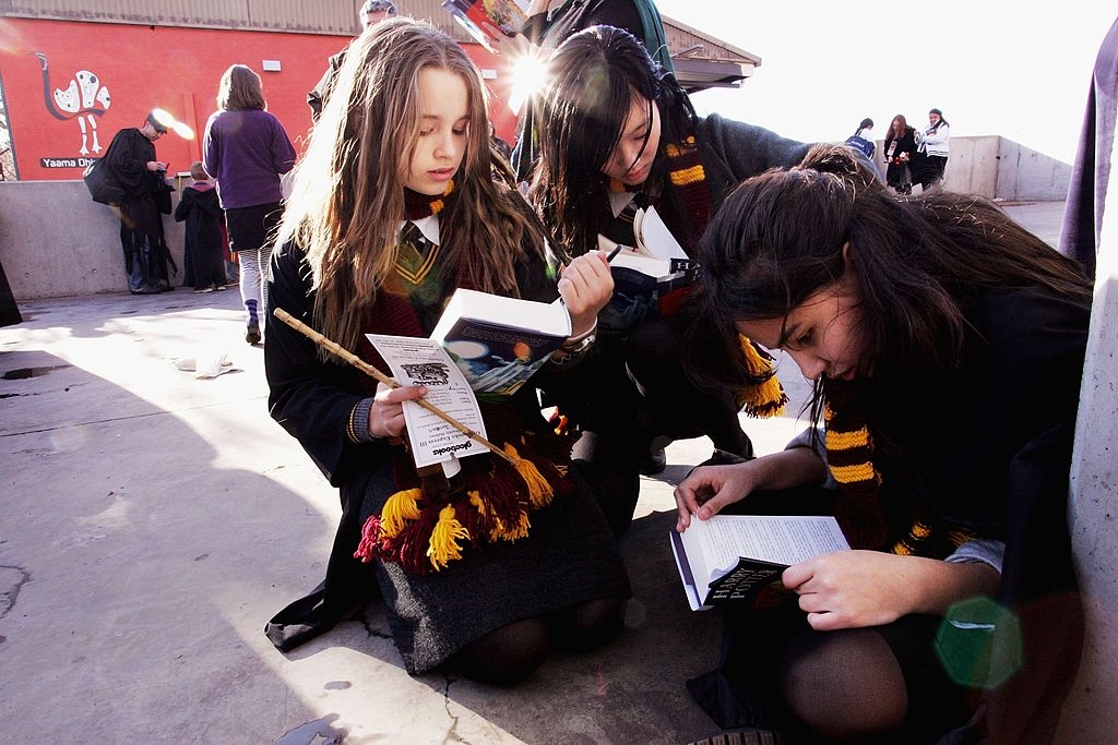 People in wizard costumes with scarves and wands read books on the ground at an event