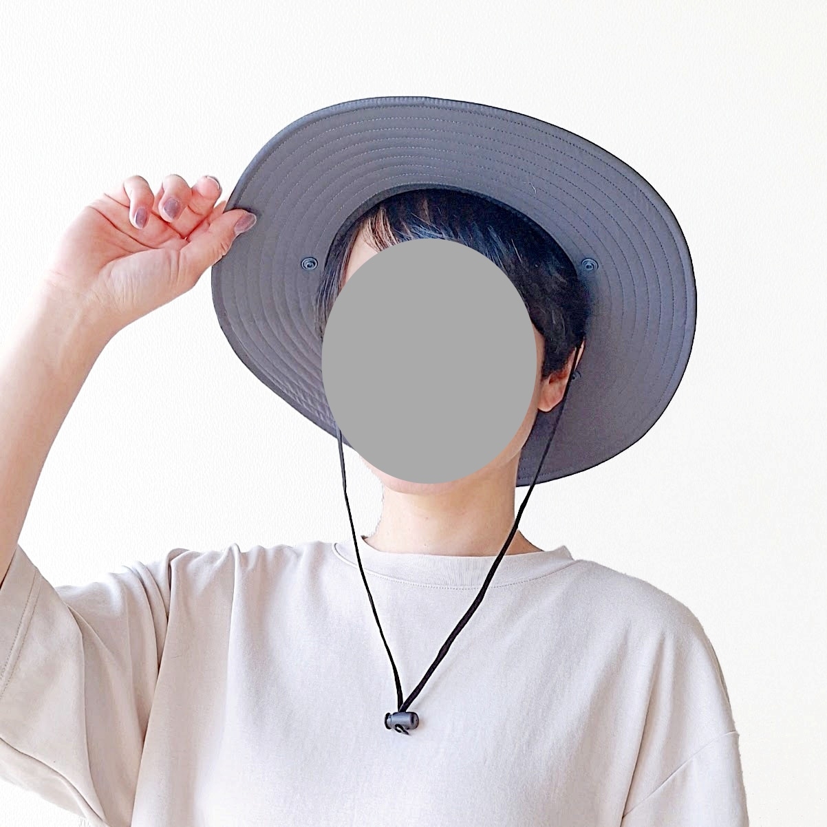人が広いつばの帽子をかぶってポーズをとっている。シンプルな服装。顔は隠されている。