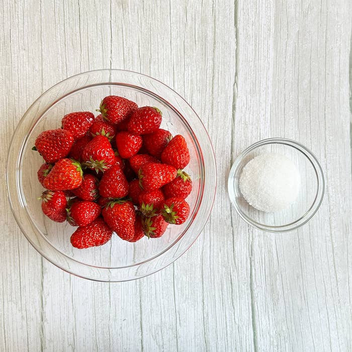 ガラスのボウルに入ったいちごと、小さなボウルに入った砂糖が白木のテーブルに置かれている。