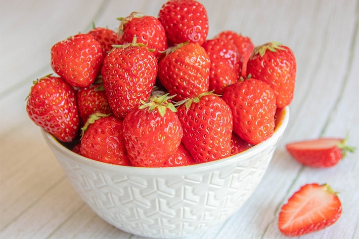 白いボウルに盛られた新鮮なイチゴがテーブルに置かれている。横に半分に切ったイチゴも見える。