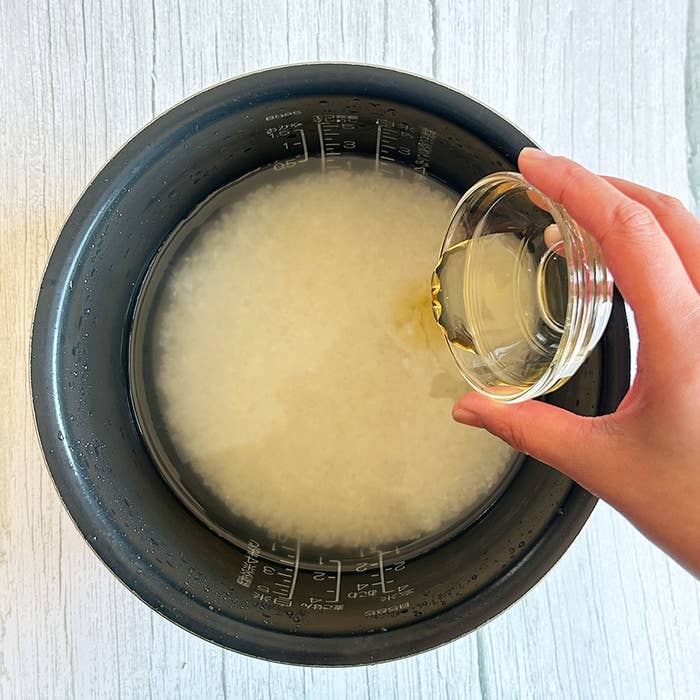 炊飯器に入った米に小さなガラス容器から液体を注いでいる手。