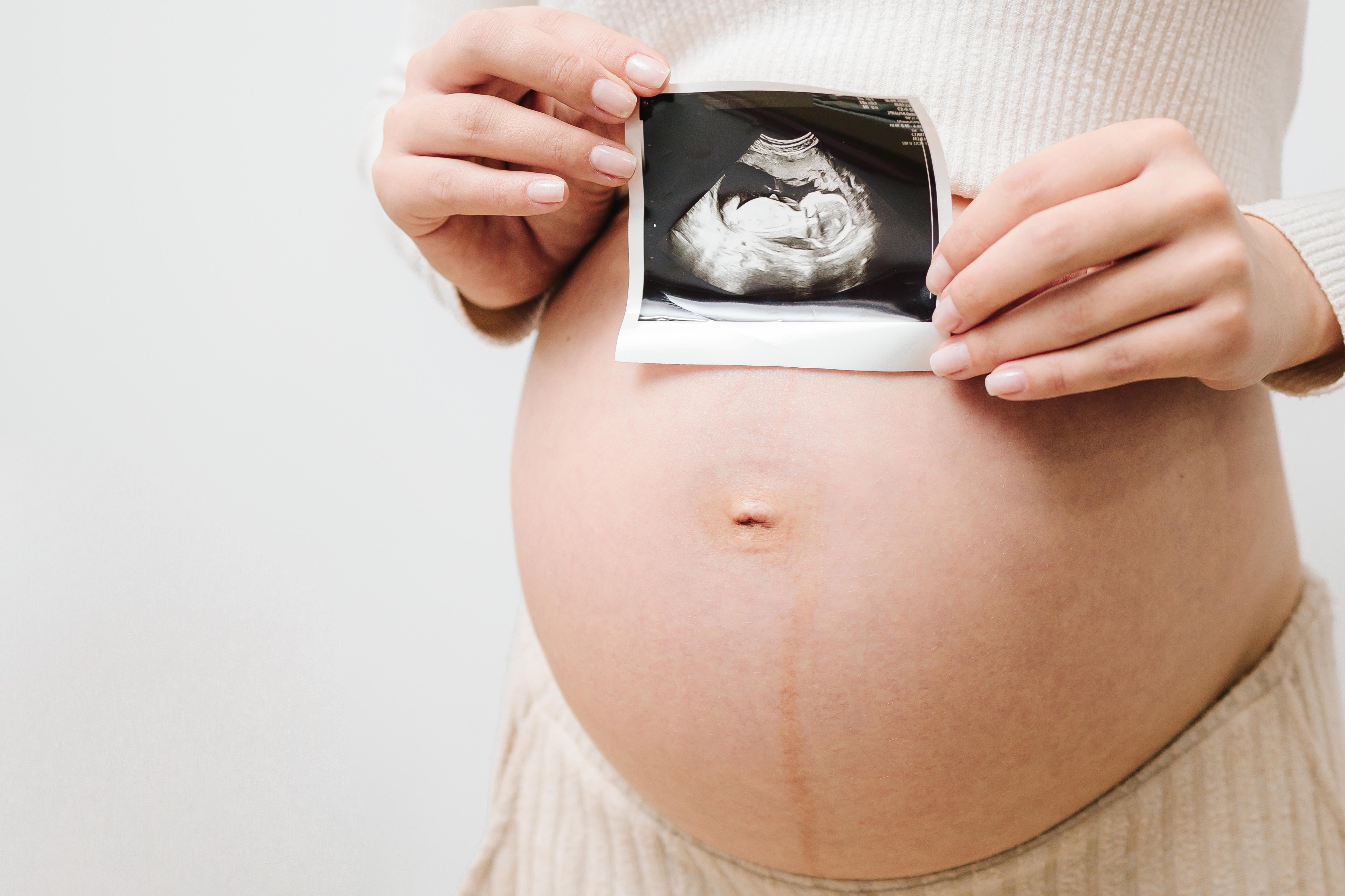 Person holds an ultrasound photo against their pregnant belly, showing the image of an unborn baby