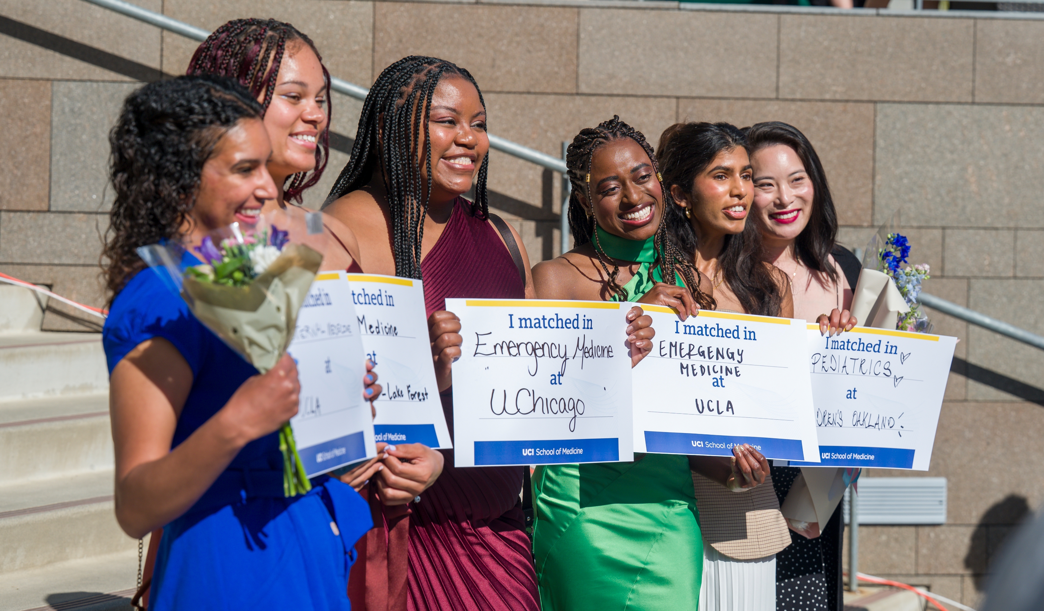 Six people smile and hold "I matched" signs showing they've been accepted into various medical schools. Some hold bouquets