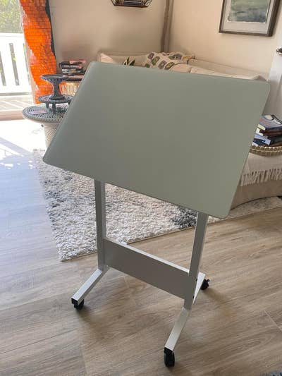 Adjustable rolling desk in a modern living room setup, featuring a soft fabric chair and cozy decor items